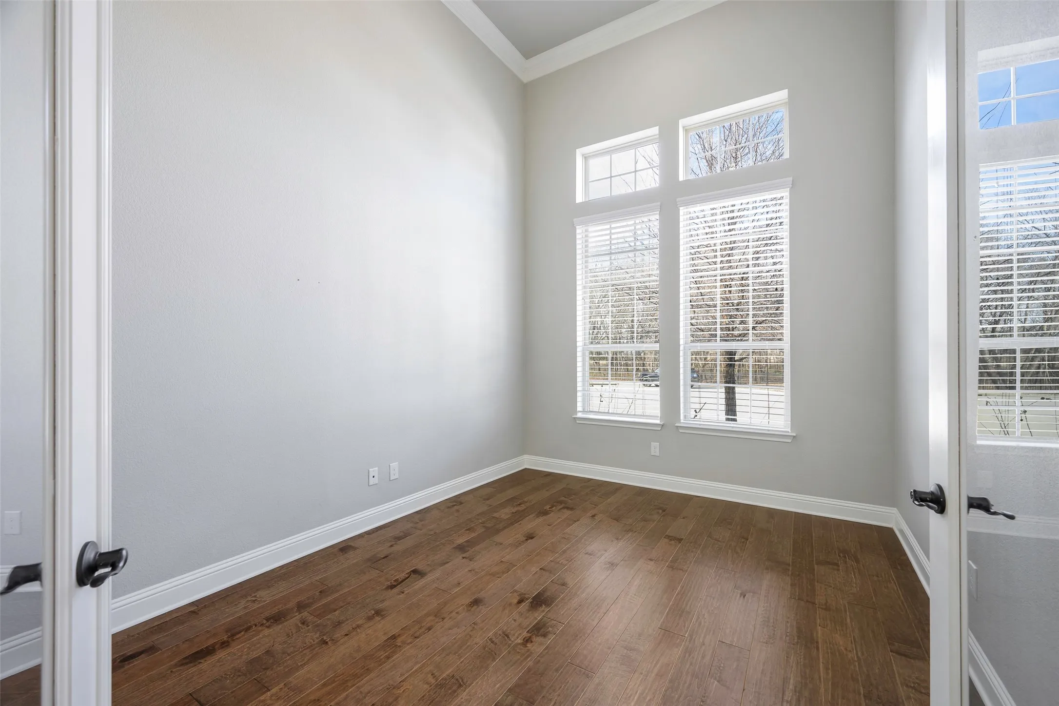 Vaulted ceiling with crown molding, wood-finish flooring, and multiple large windows with blinds