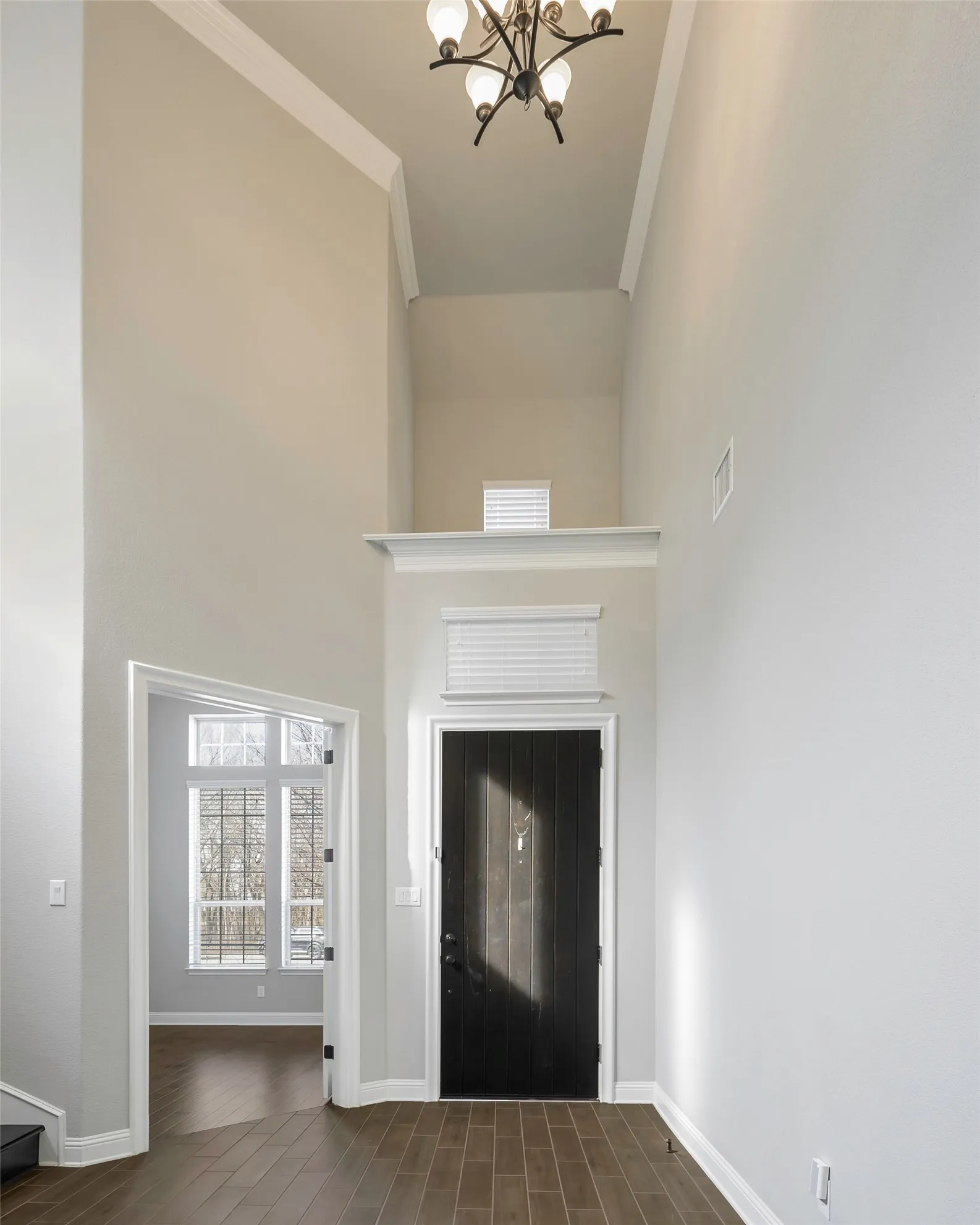 Soaring ceilings with crown molding, dark wood-finish flooring, a dark paneled entry door, an upper window, and a chandelier