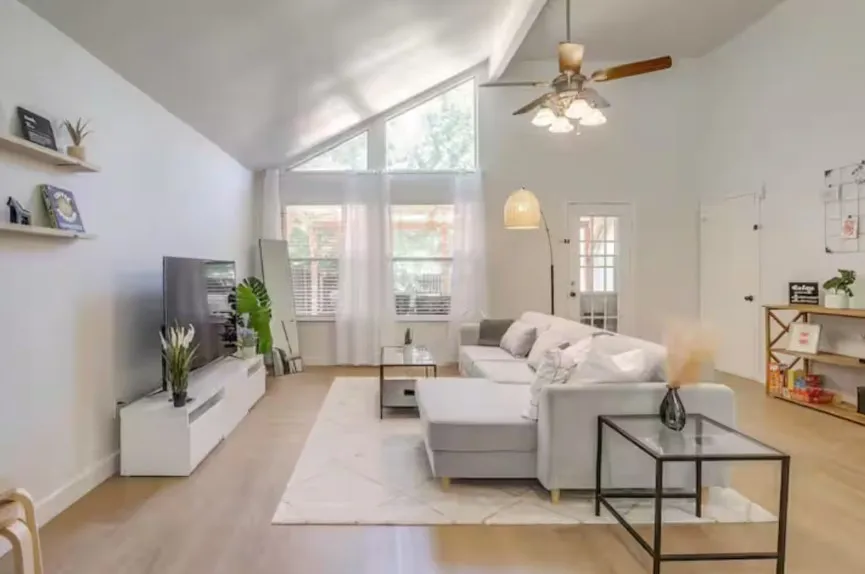 Vaulted ceilings with an exposed beam, a ceiling fan with integrated lighting, wood-finish flooring, and large windows