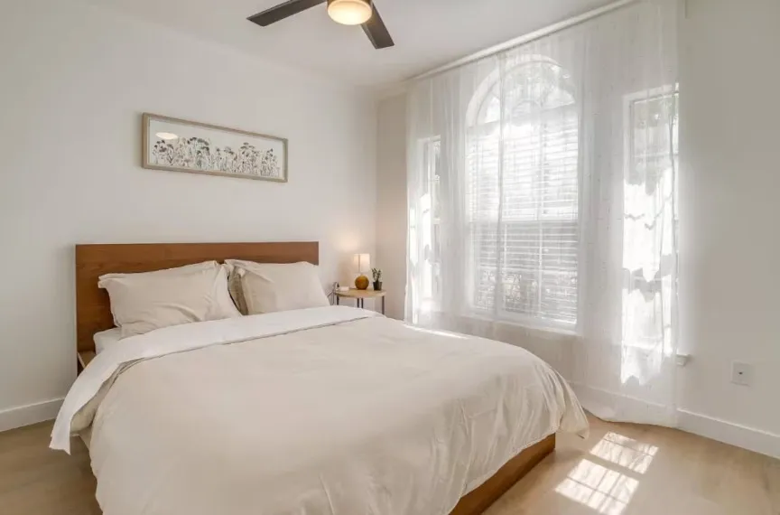 Arched window with blinds and sheer drapery, wood-finish flooring, and a ceiling fan