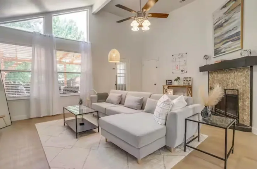 Vaulted ceilings, a ceiling fan, wood-finish flooring, a fireplace with a black mantel, and a French door