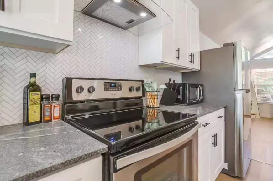 Kitchen featuring white cabinetry with dark hardware, a herringbone pattern tile backsplash, and a stainless steel appliance suite