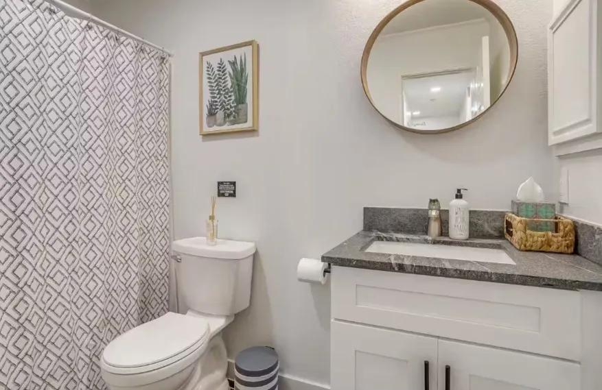 White vanity with dark stone-finish countertop, undermount sink, and black hardware