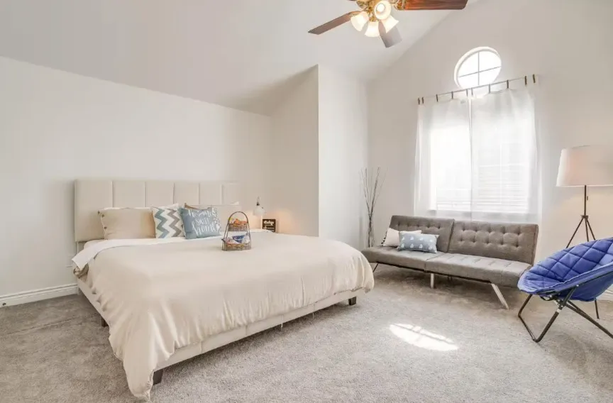 Vaulted ceiling with a ceiling fan, broad window with treatments, circular transom window, and light-toned carpet flooring