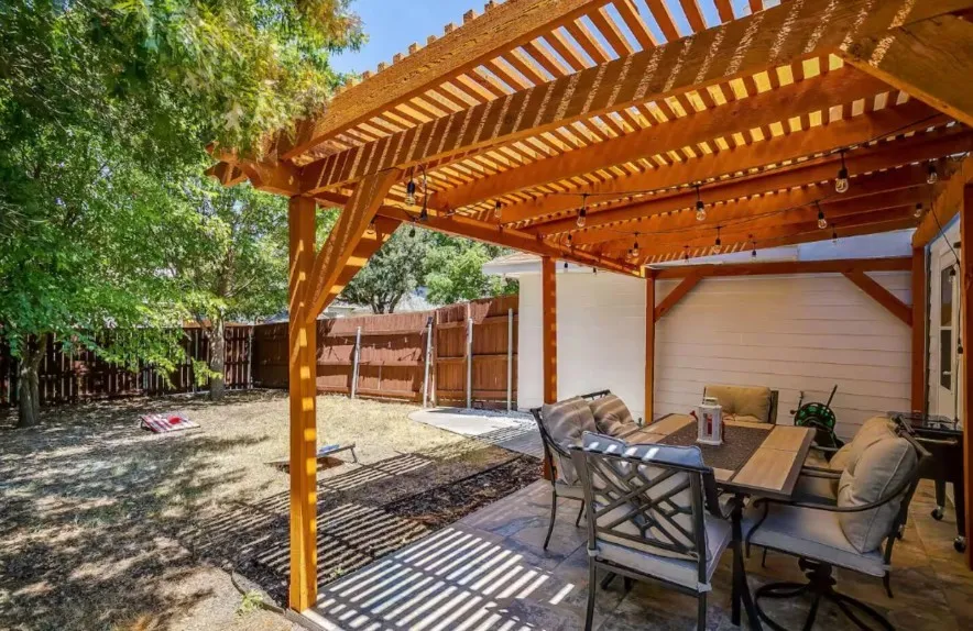 Expansive backyard featuring a wood pergola, string lighting, and a paved patio area