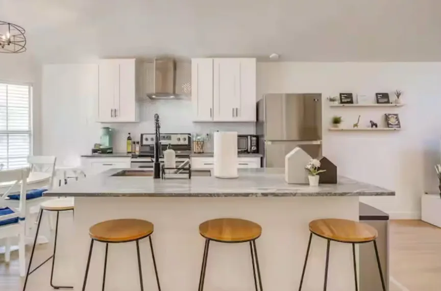 Kitchen featuring an island with an undermount sink, stainless steel appliances, white cabinetry, and wood-finish flooring