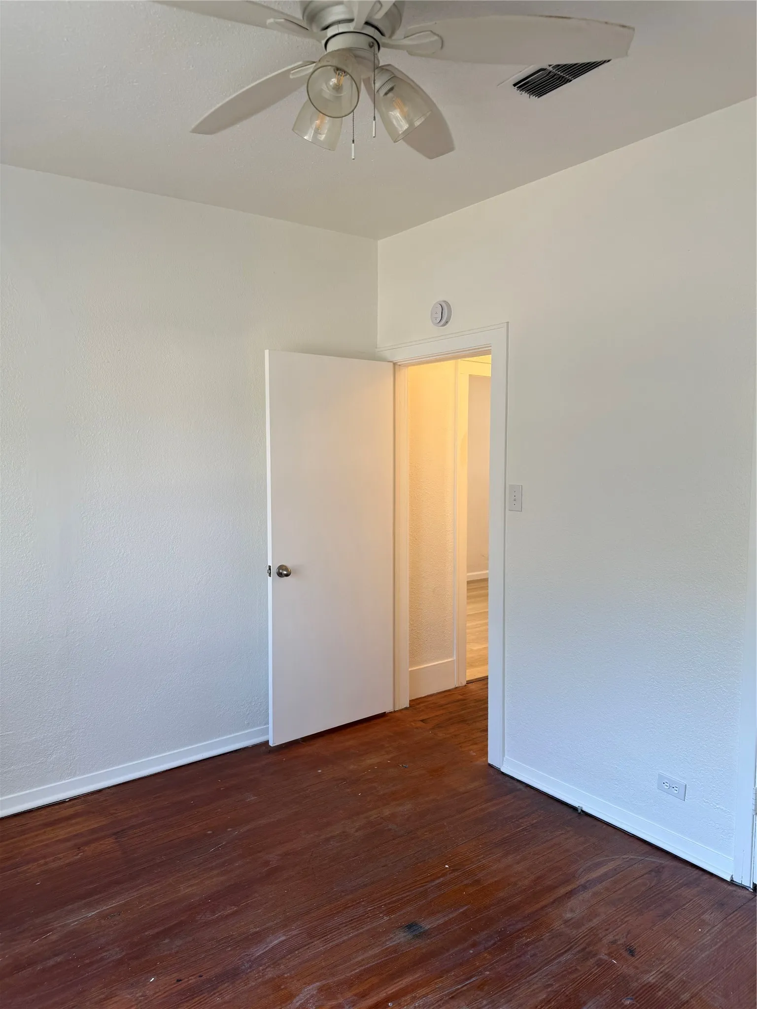 Spacious bedroom with hardwood flooring, ceiling fan with integrated lighting, and direct access to an adjoining room