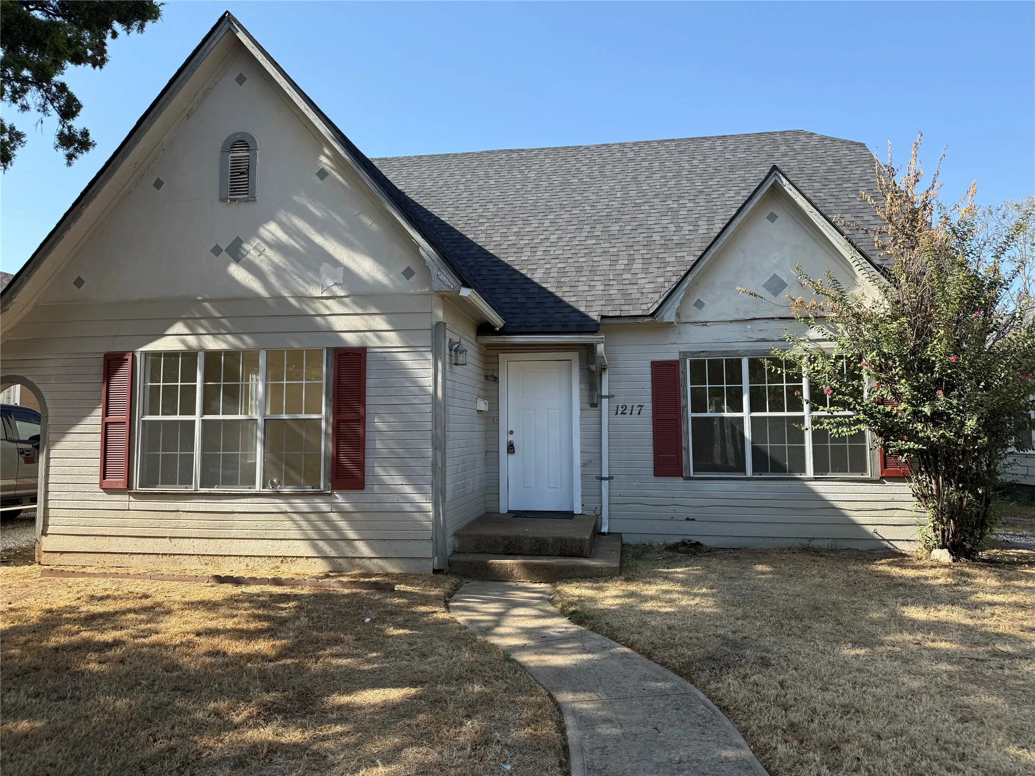 Gable roofline with shingle roofing, front facade with horizontal siding, front entry door with transom window, decorative shutters, and a concrete pathway leading to the entrance