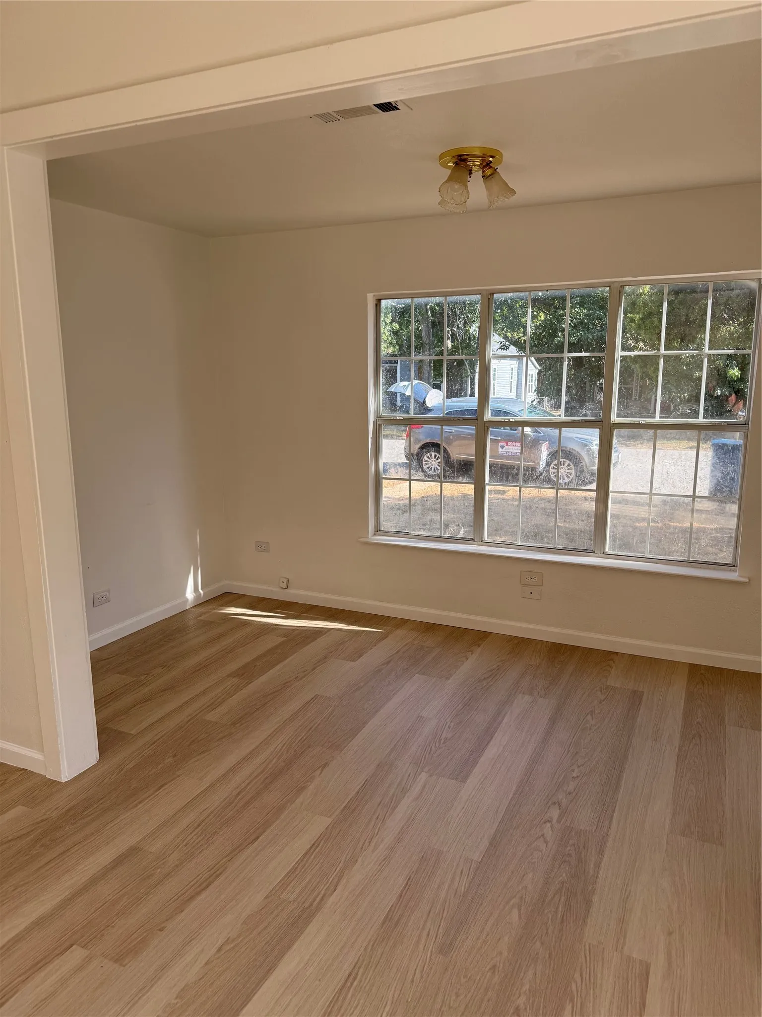 Wood-finish flooring, white wall paint, window with grid panes, and a flush mount ceiling light