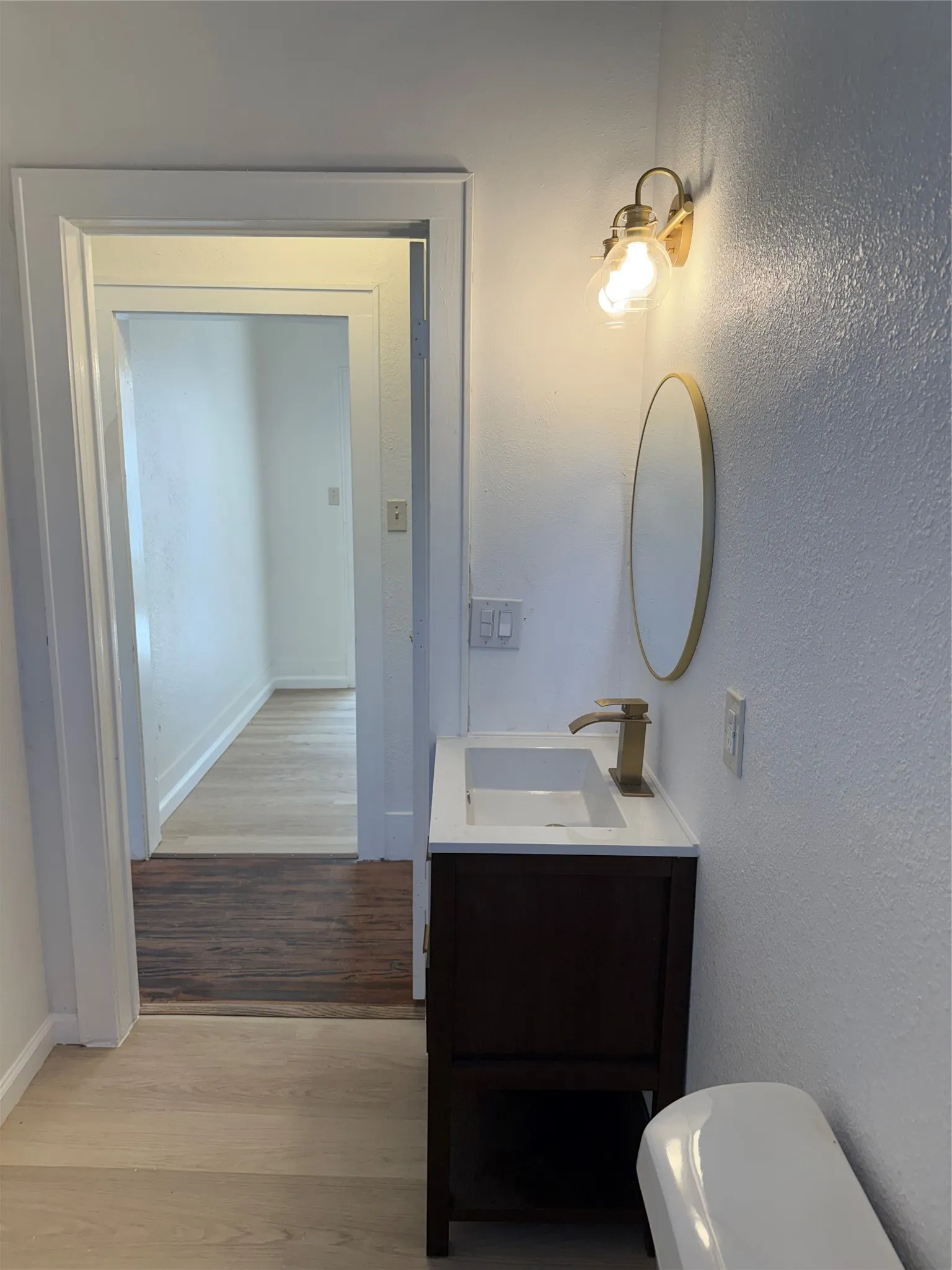 White vanity with a rectangular basin, gold-finish faucet, and coordinating oval mirror