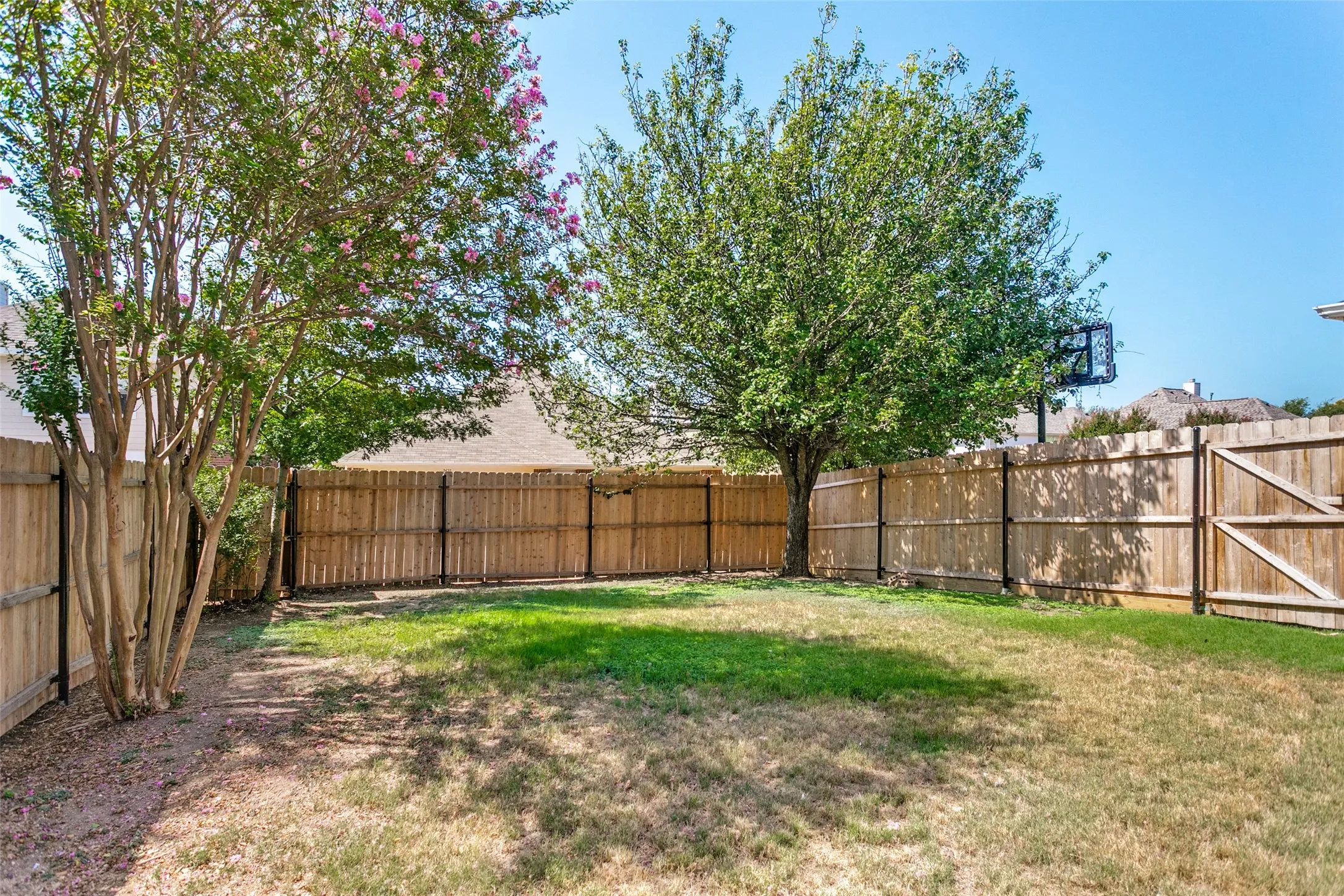 Spacious backyard retreat featuring a manicured lawn, mature shade trees with spring blooms, and sturdy wood-finish fencing
