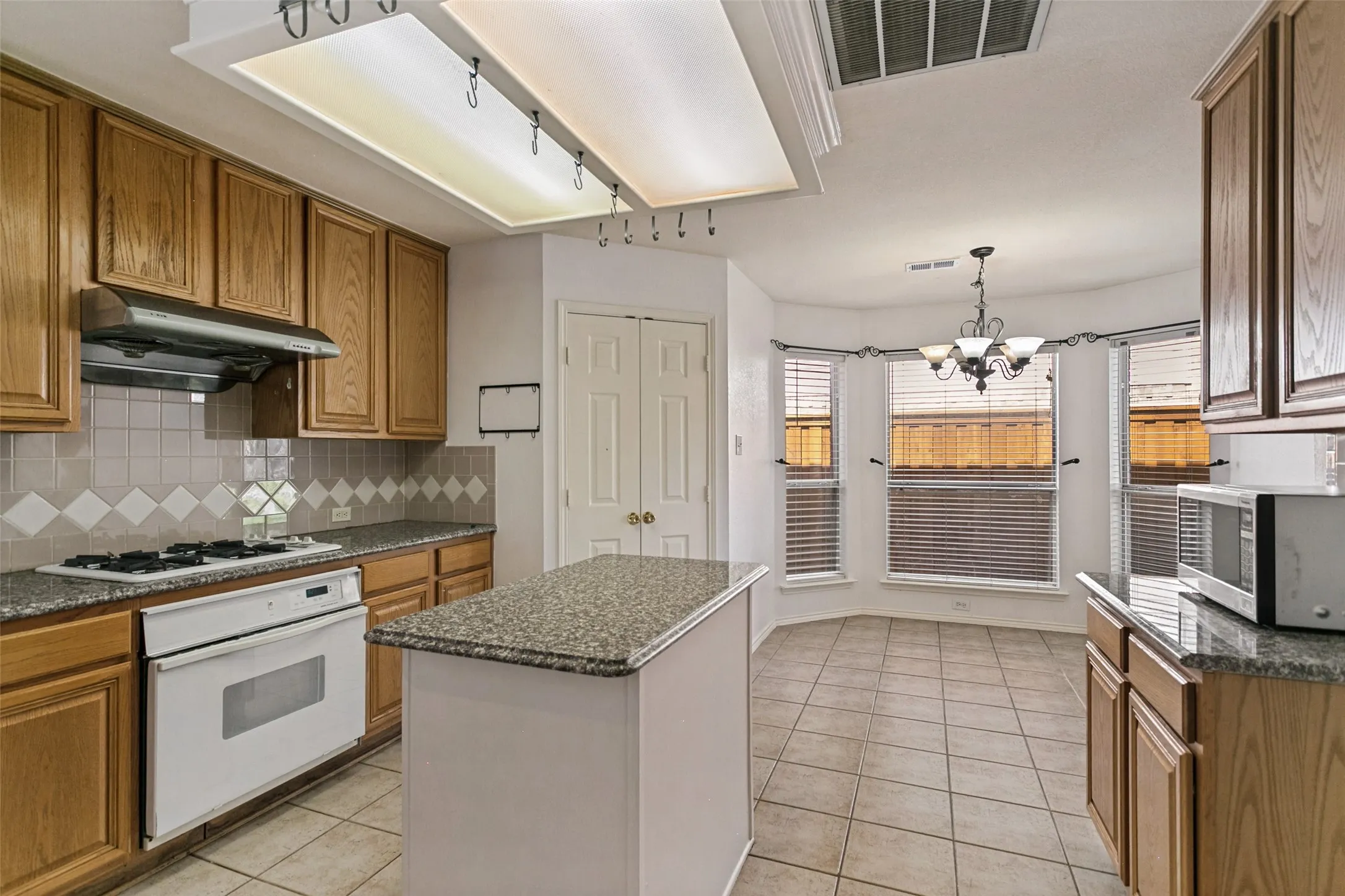 Kitchen featuring a central island, recessed lighting, tile flooring, wood cabinetry, and a bay window dining area