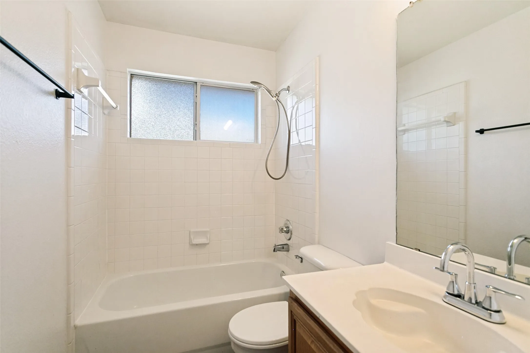 White tile bath/shower combination with a frosted glass window, single vanity with a laminate countertop, and a large wall-mounted mirror
