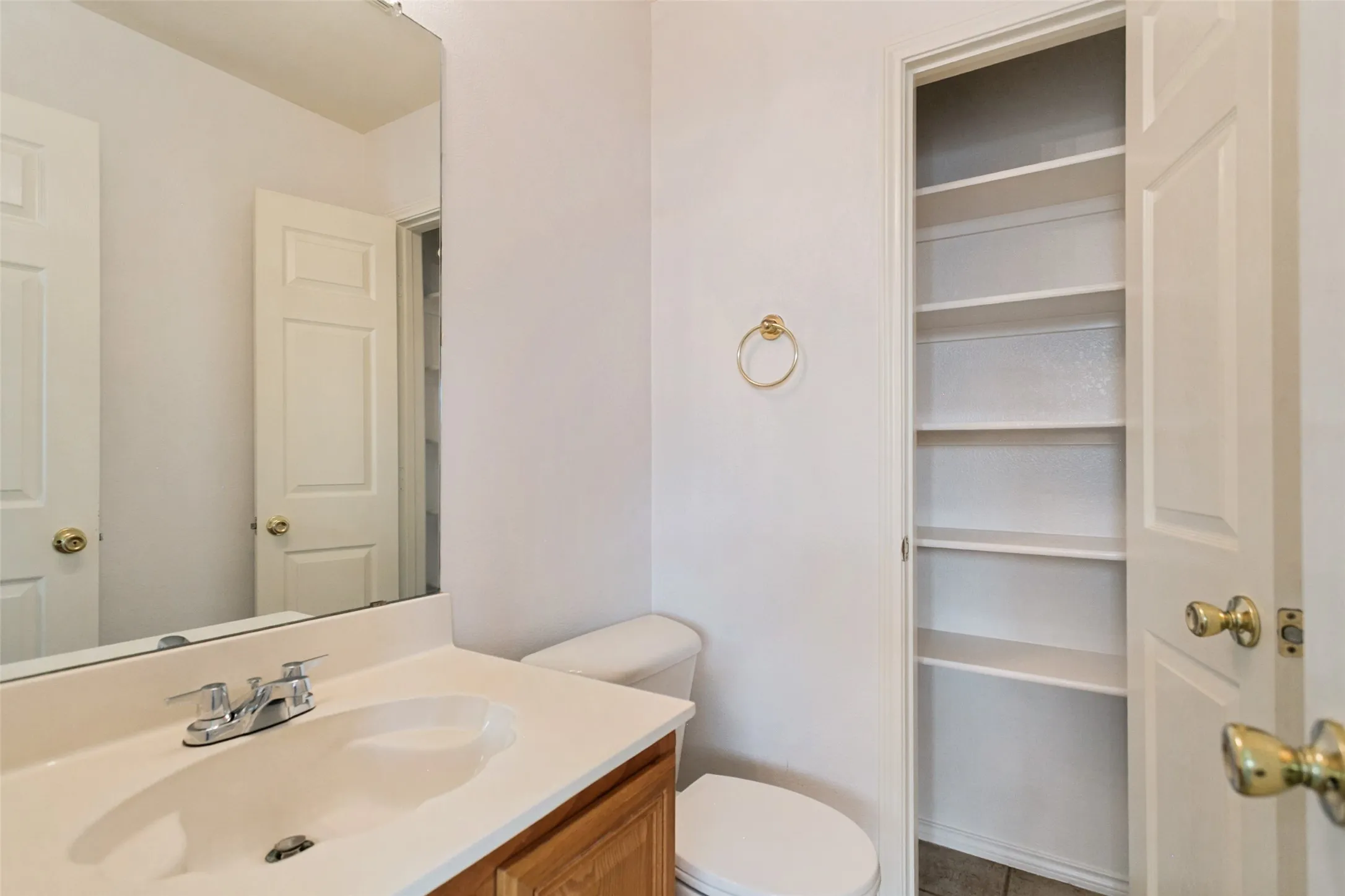 Bathroom featuring a vanity with an integrated sink, polished chrome faucet, wood-finish cabinetry, and a built-in linen closet with shelving