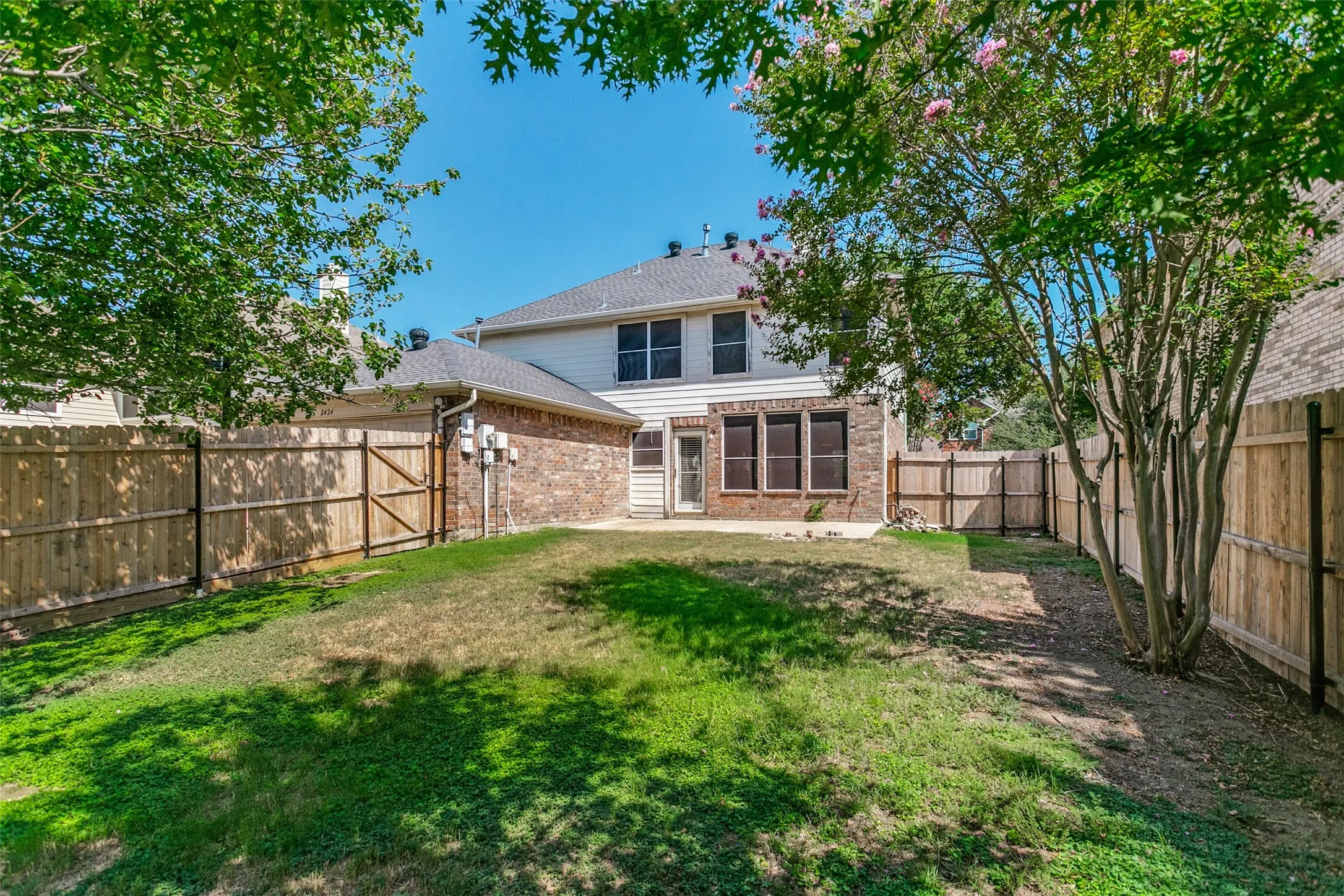 Expansive backyard featuring a privacy fence, brick exterior, and a paved patio