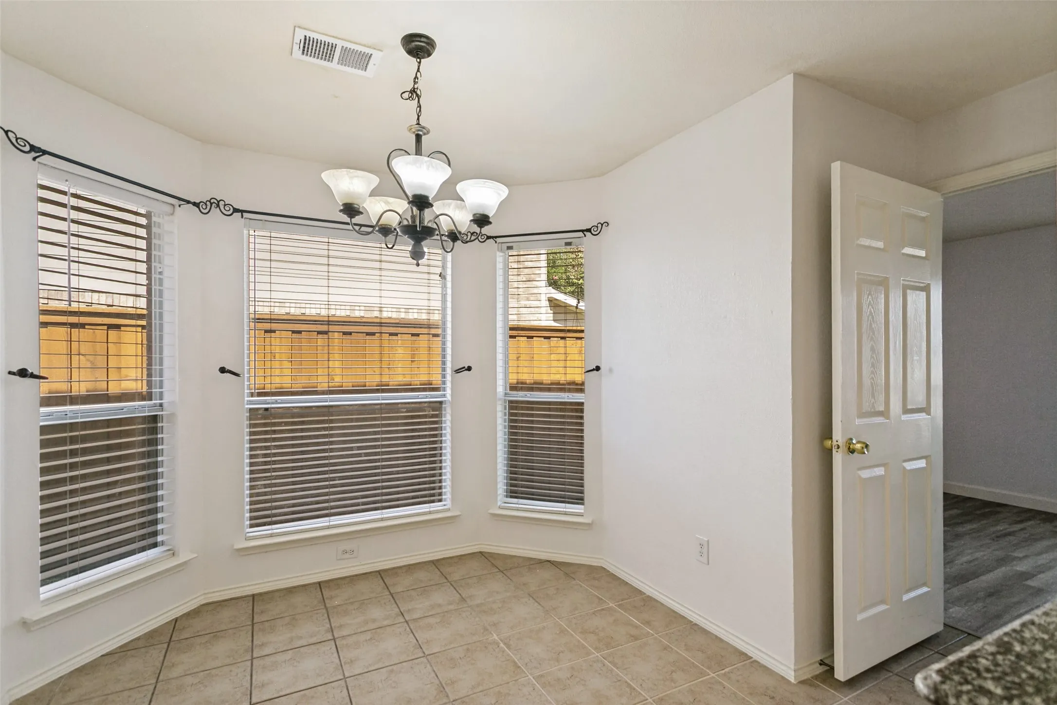 Bay window with blinds, tile flooring, and overhead chandelier