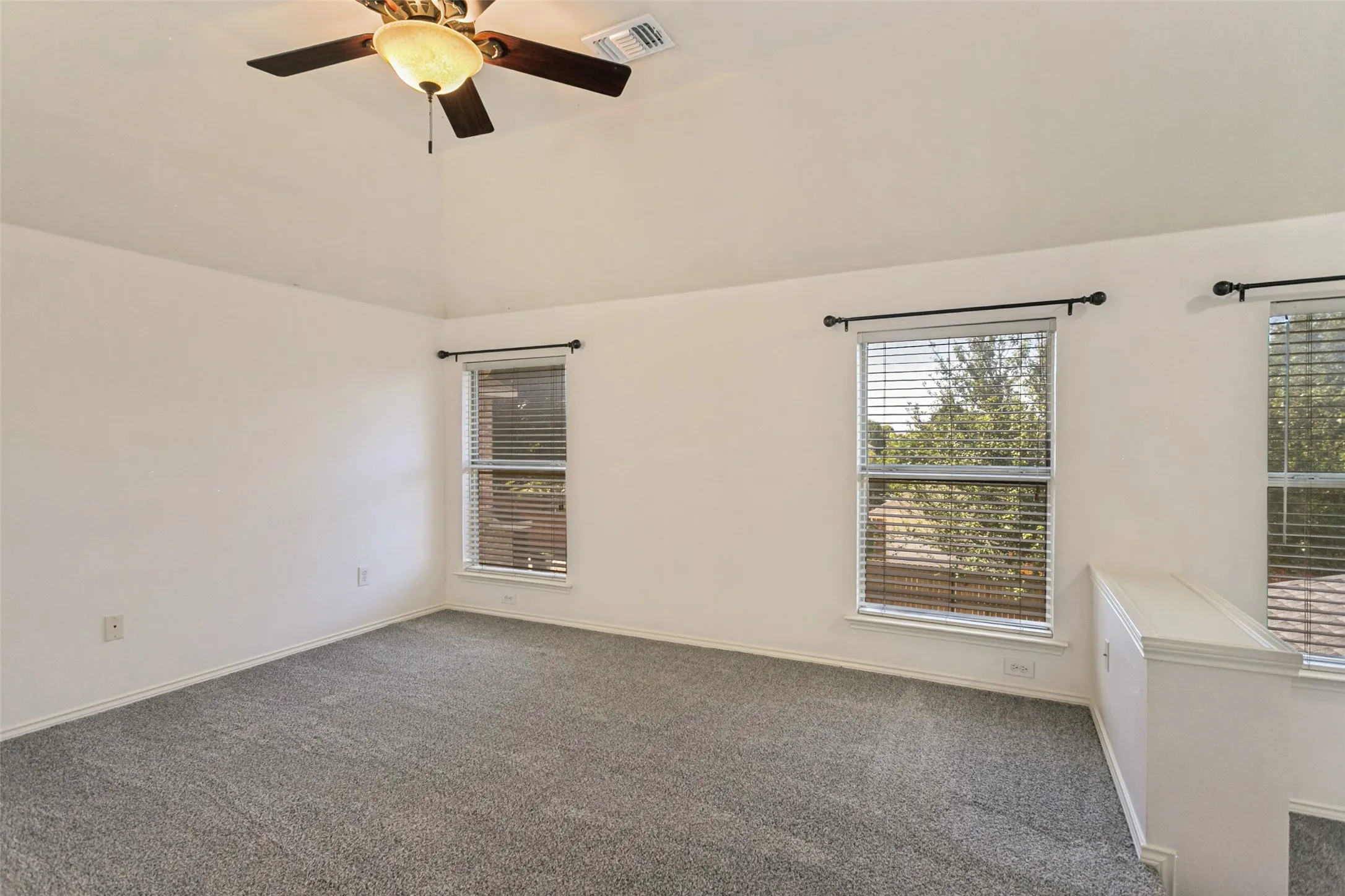 Vaulted ceiling with a ceiling fan, gray carpeting, two windows with blinds, and white wall finishes