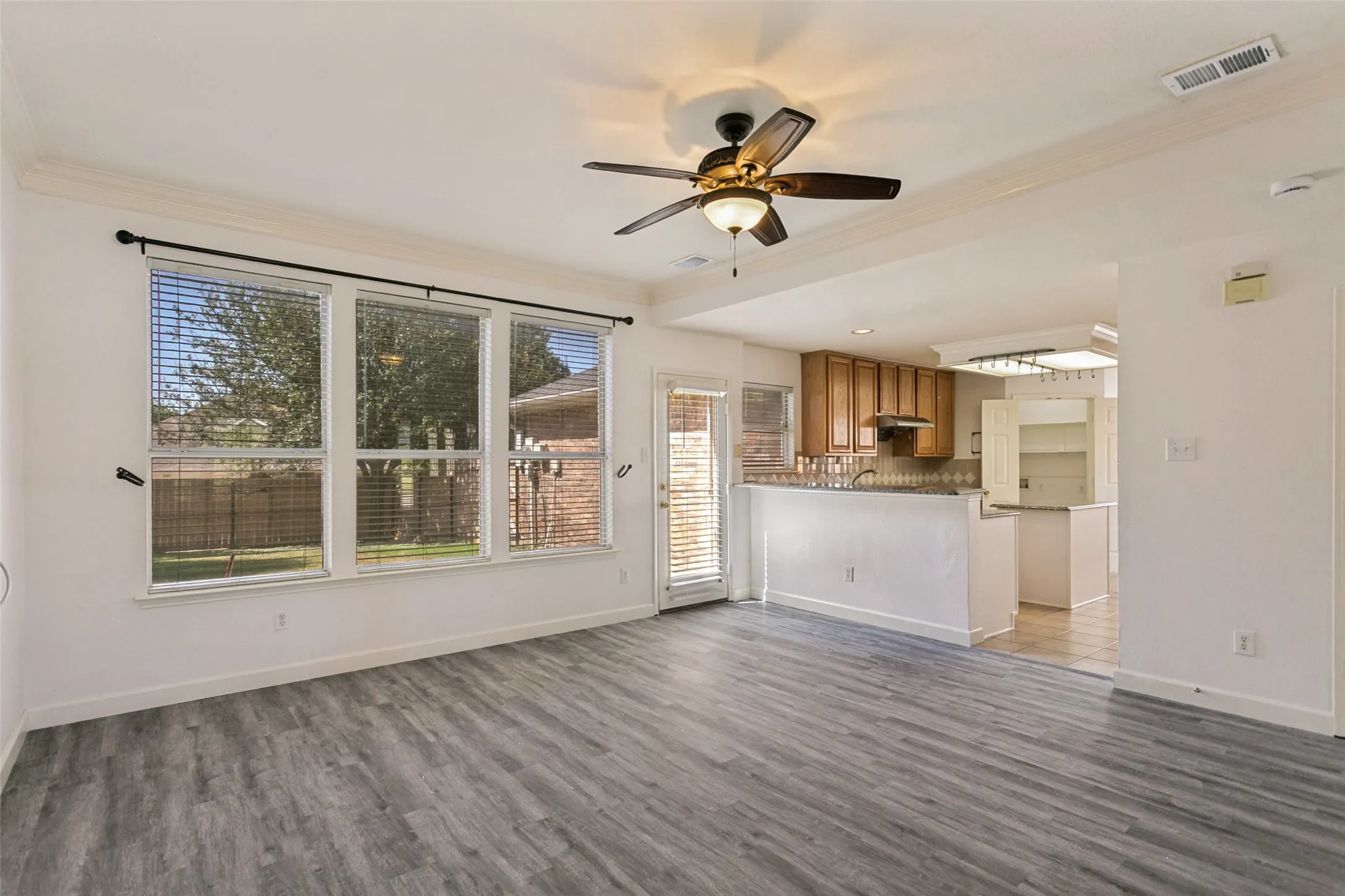 Laminate wood-finish flooring, white crown molding, recessed lighting, and a ceiling fan with light fixture