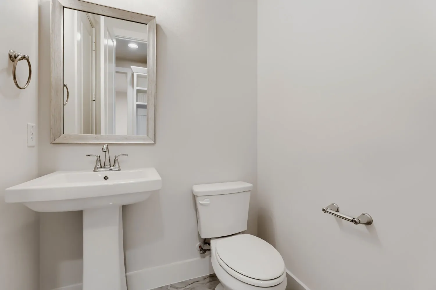 Pedestal sink with chrome faucet, framed mirror, and toilet with a closed lid
