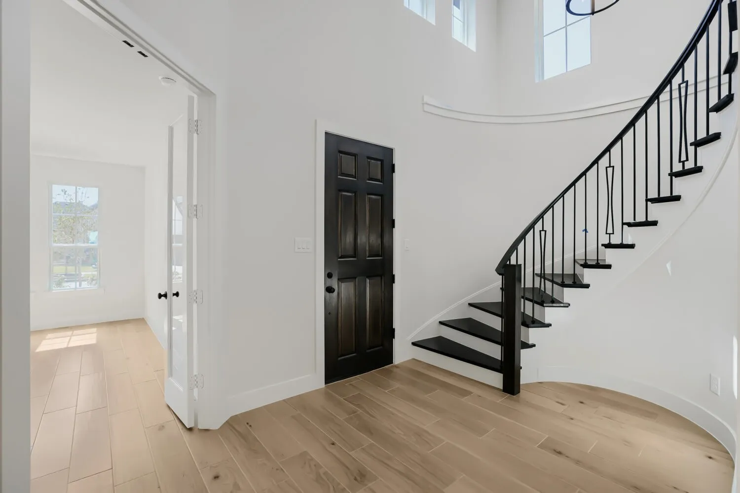 Curved staircase with black metal balusters, wood-finish flooring, white walls, dark paneled door, and French doors