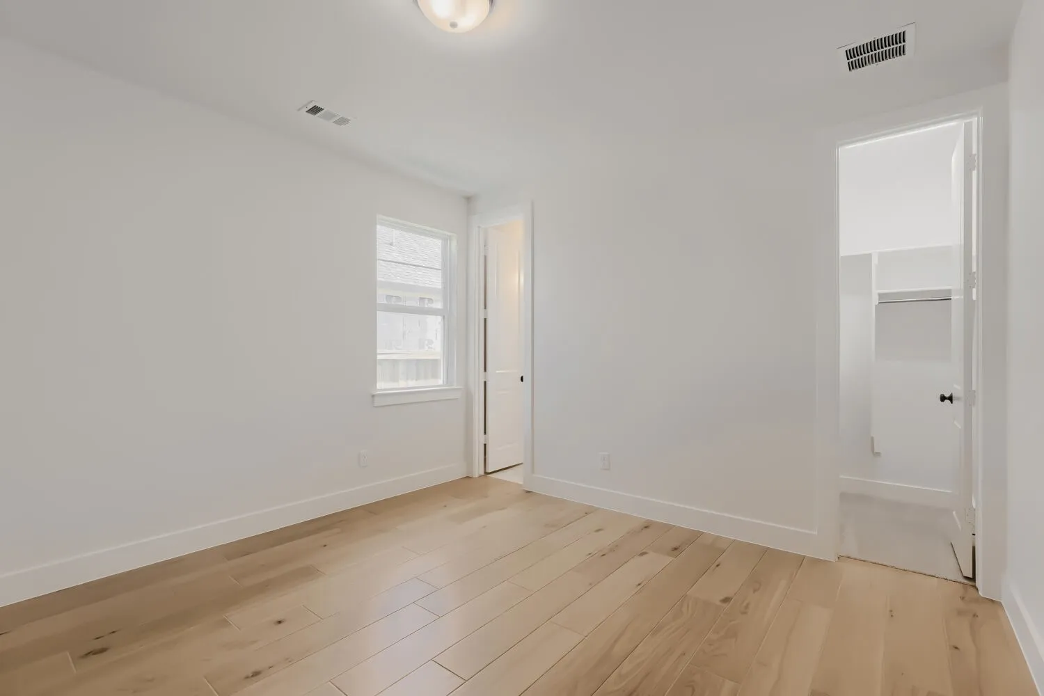 Light wood-finish flooring, white walls, a single window, and a recessed ceiling light fixture
