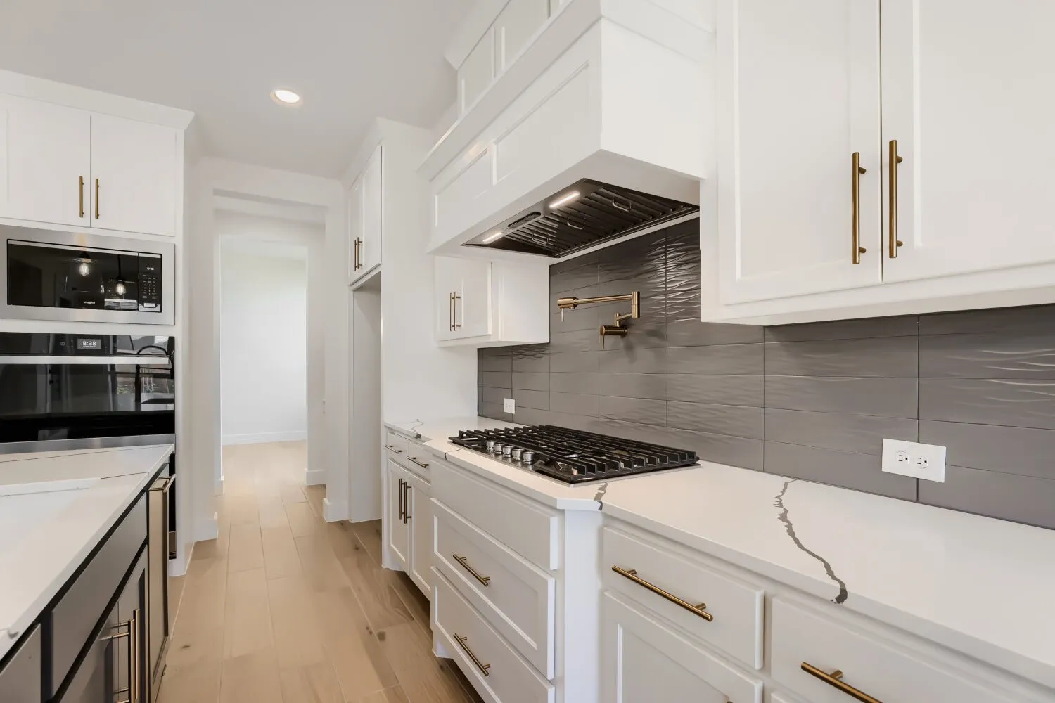 White shaker cabinetry, light wood-finish flooring, built-in stainless steel appliances, patterned gray tile backsplash, and white countertops with gray veining
