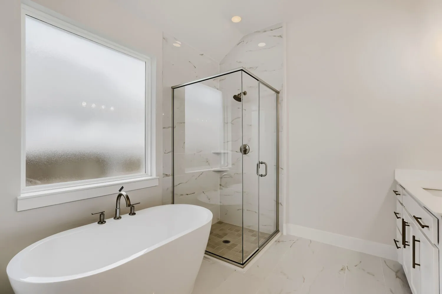 Freestanding soaking tub with dark bronze fixtures, frosted window, corner glass shower with tile surround, white cabinet vanity with dual sinks, and large format floor tile