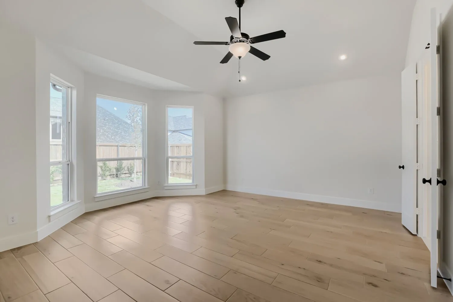 Vaulted ceiling with a ceiling fan, recessed lighting, wood-finish flooring, and a bay window