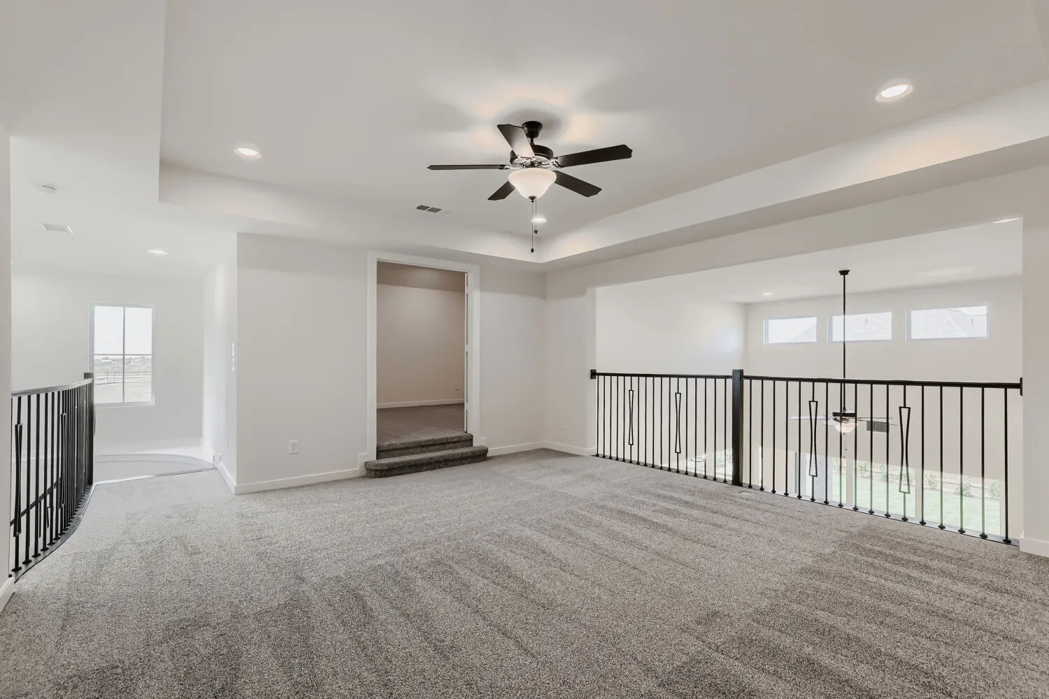 Expansive carpeted loft with recessed lighting, a ceiling fan, and wrought iron railings