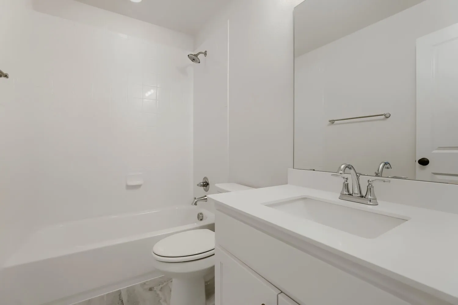 Bathroom with a white bathtub, tiled shower surround, toilet, and vanity featuring a white countertop with an integrated sink and chrome faucet