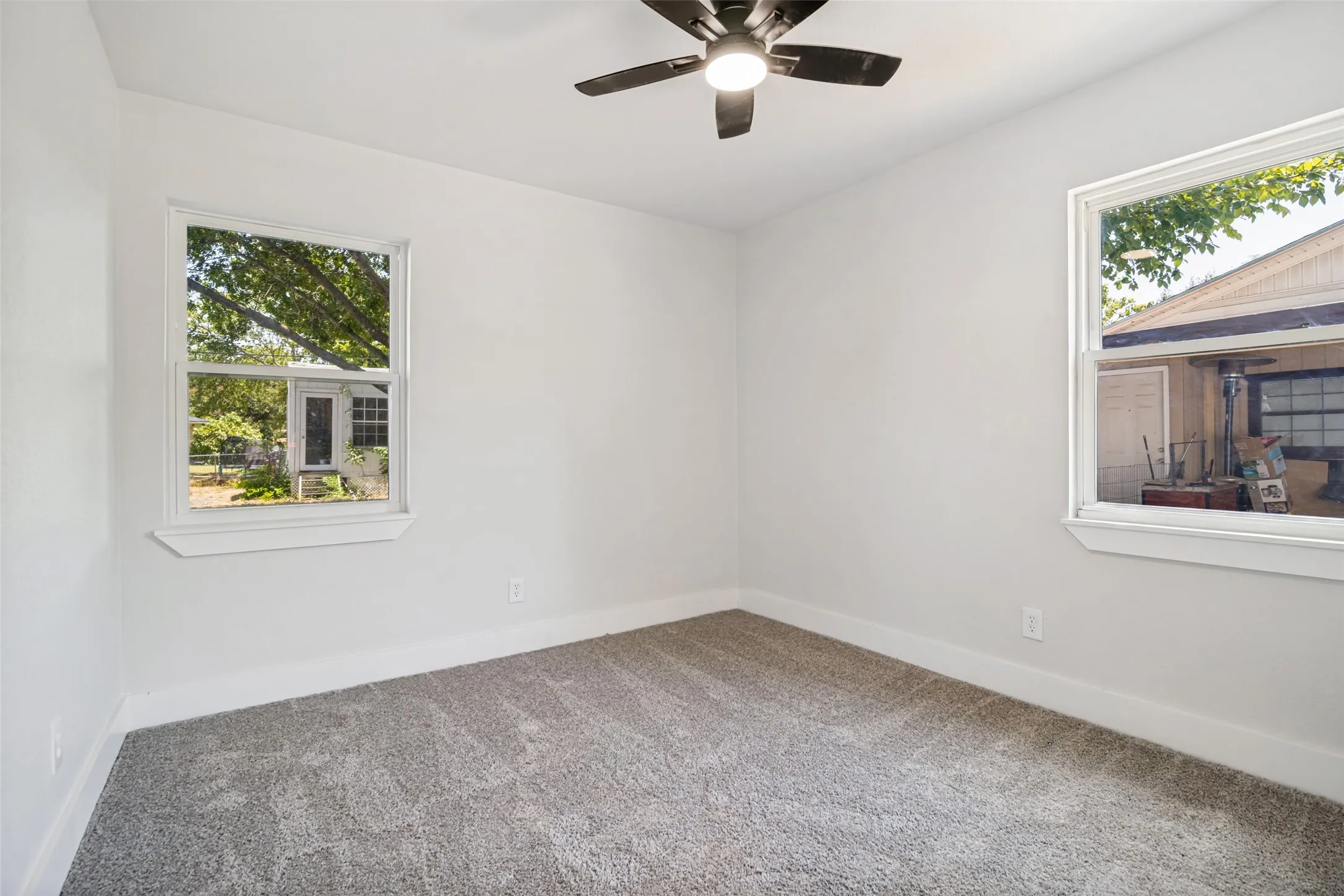 Neutral wall paint, ceiling fan with integrated lighting, two windows, and gray carpet flooring