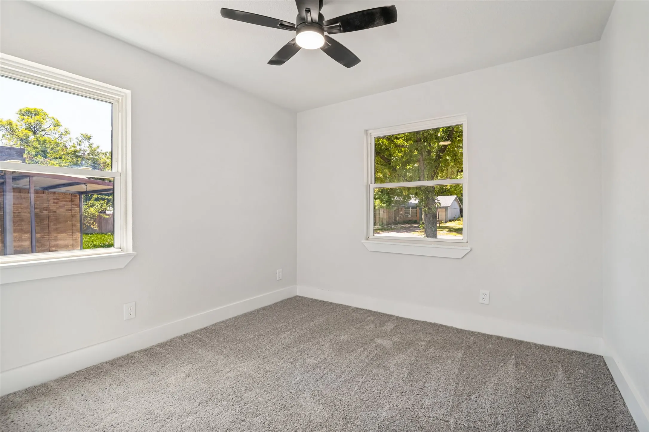 Bright room with two windows, a ceiling fan with integrated lighting, and gray carpeting