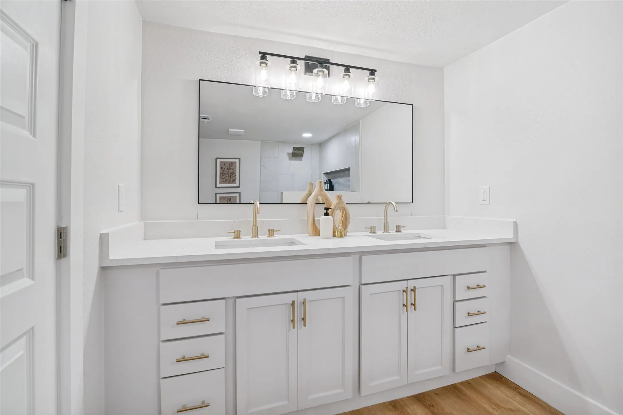 Dual vanity with integrated sinks, white cabinetry, brass hardware, and a large framed mirror