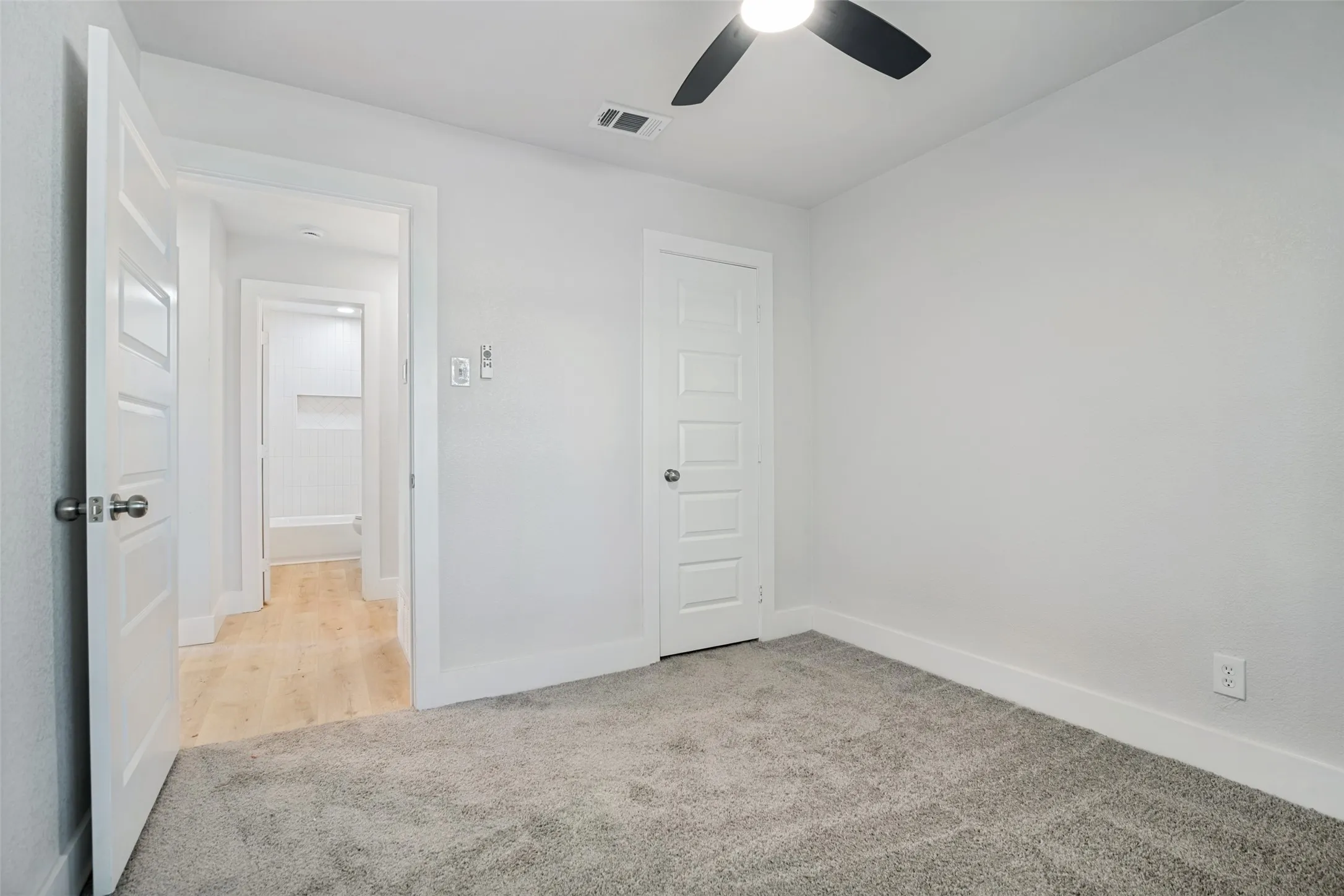 Carpeted flooring, ceiling fan with integrated lighting, paneled interior doors, and light wood-finish flooring visible in the hallway