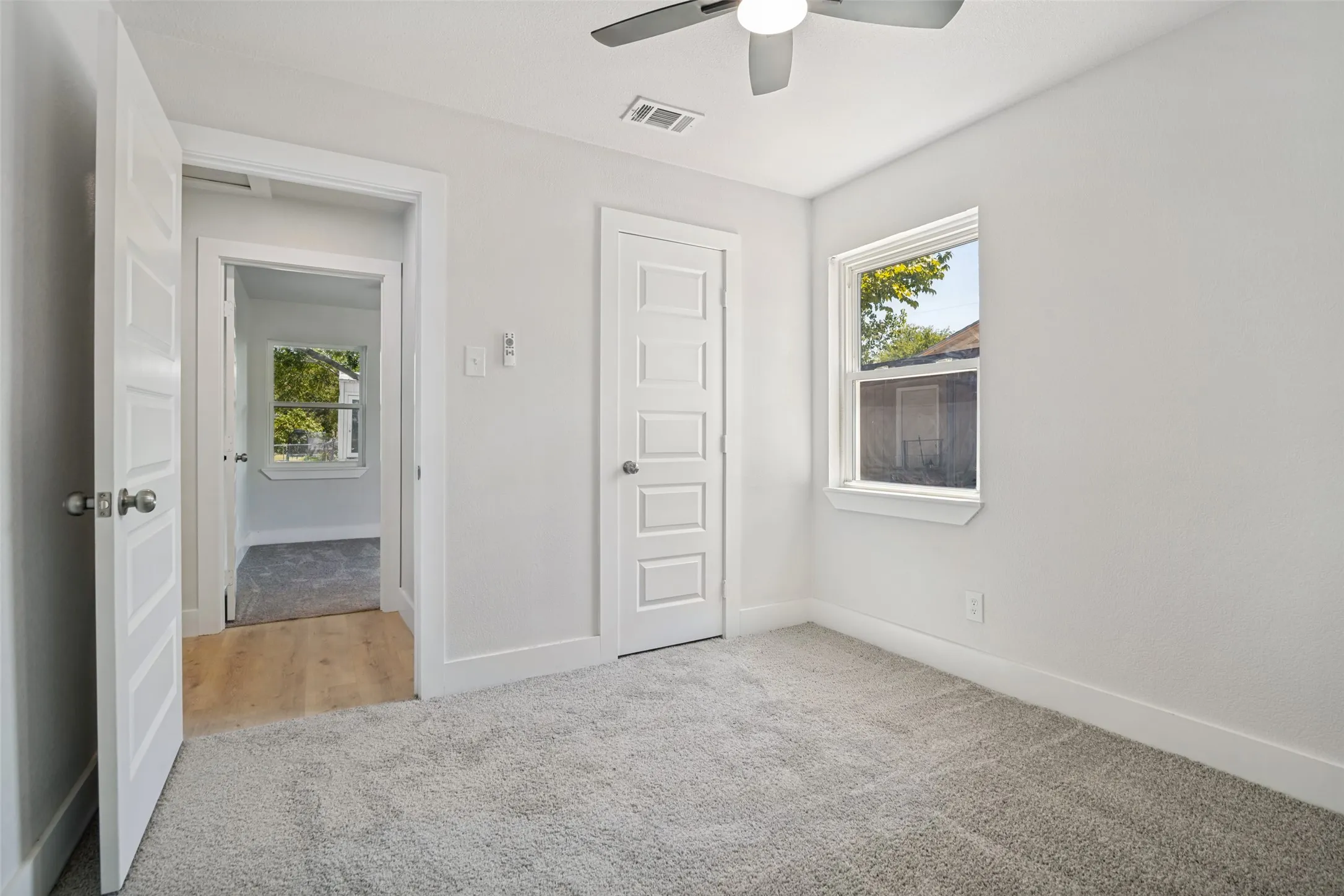 Light-colored carpeting, white walls, and a ceiling fan with integrated lighting