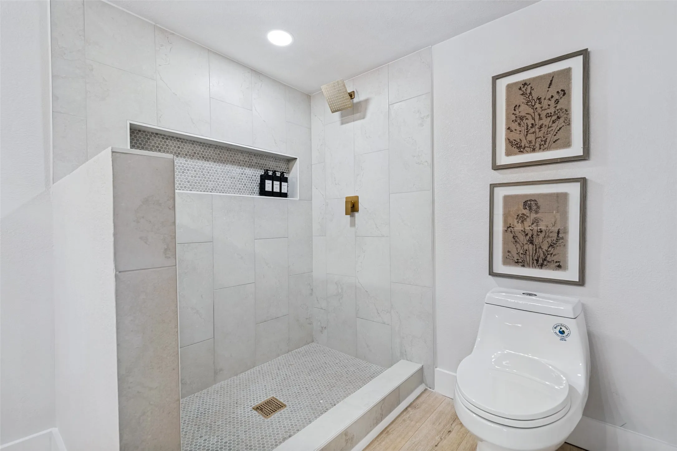 Tiled shower enclosure featuring a recessed niche with mosaic tile backing, a gold-toned shower fixture, and a gold-toned shower head