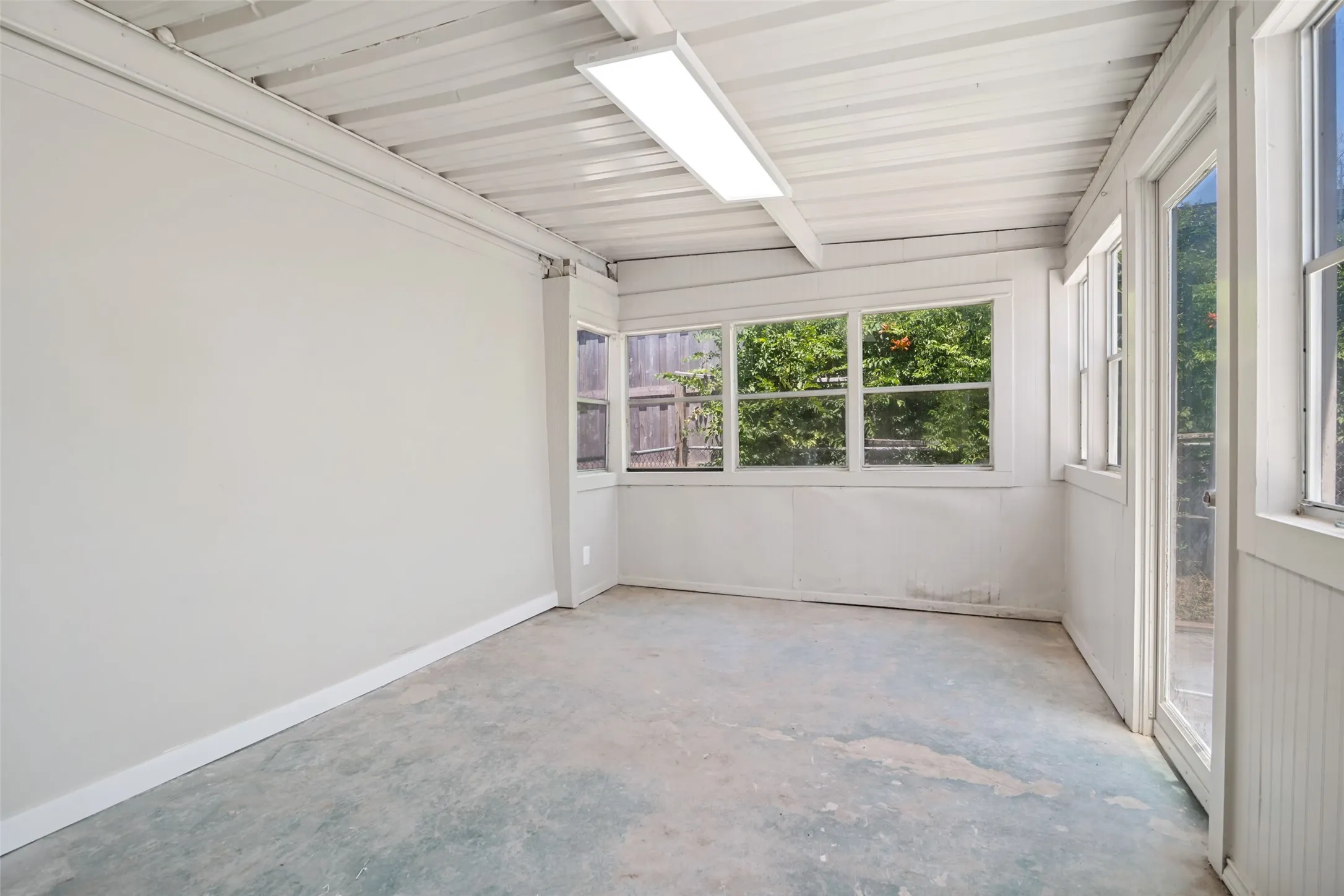 Enclosed patio space featuring multiple windows, a concrete floor, and a corrugated metal ceiling with a flush-mount light fixture