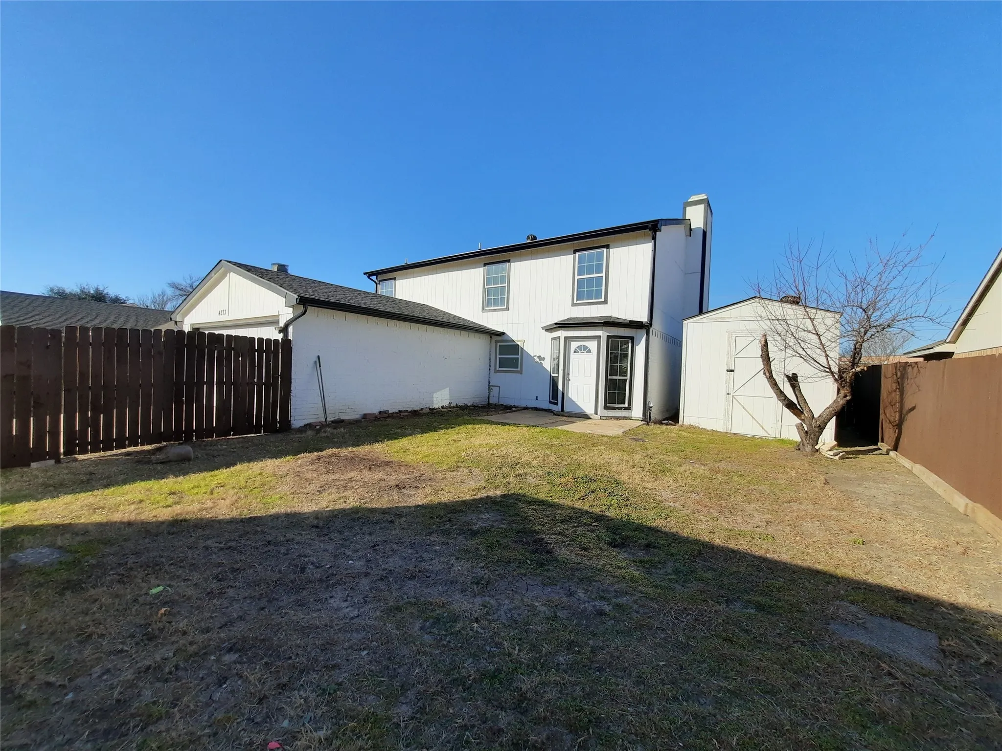 White siding exterior with black trim, fenced yard, and an exterior storage shed
