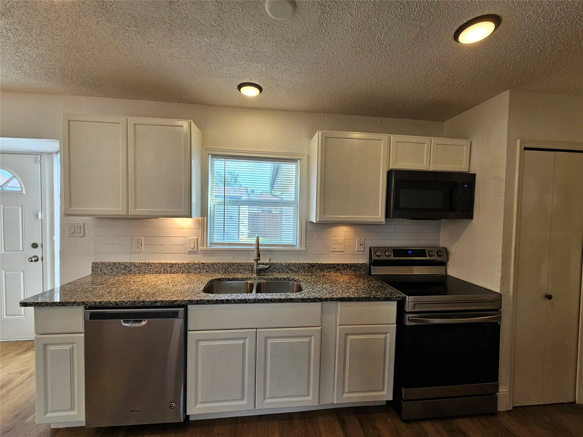 Kitchen featuring white cabinetry, granite countertops, stainless steel appliances, a double basin sink, and wood-finish flooring