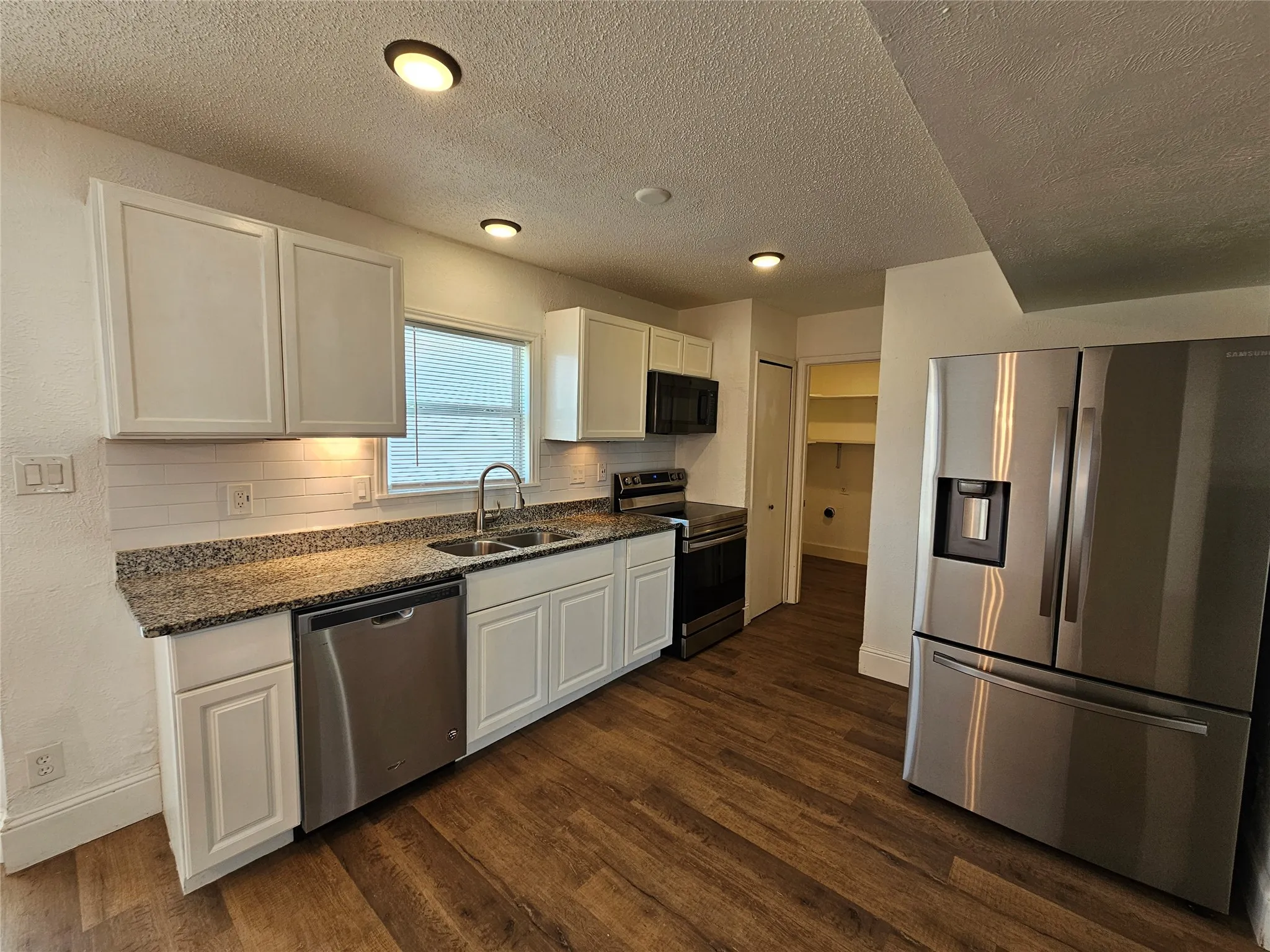 Kitchen featuring wood-finish flooring, white cabinetry, granite-style countertops, and stainless steel appliances