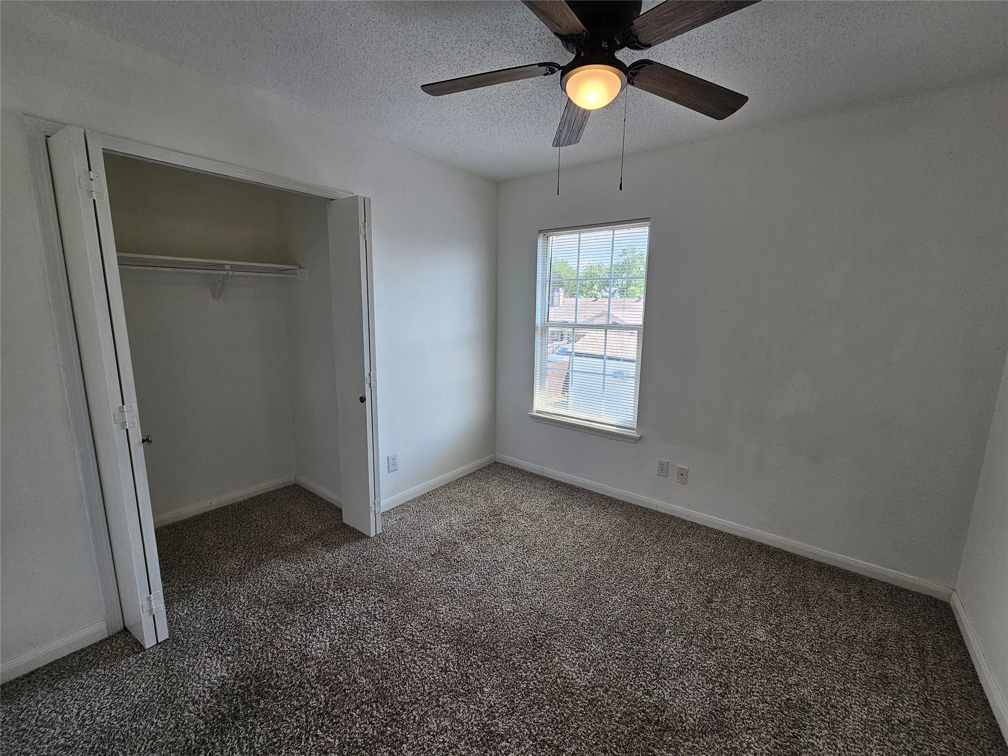 Carpeted room featuring a ceiling fan with integrated lighting, a window, and a bi-fold door closet