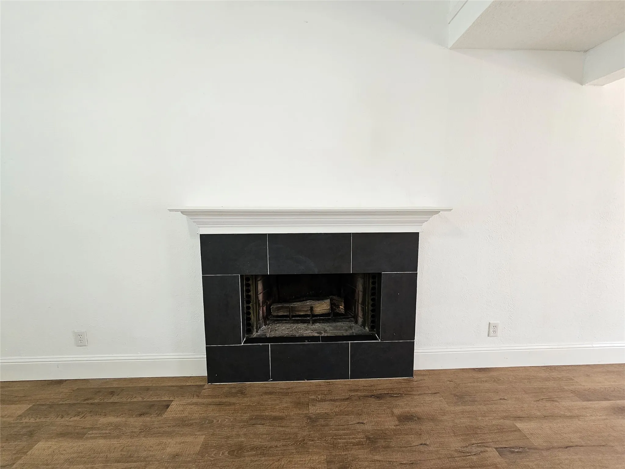 Fireplace featuring dark tile surround, white mantel, and wood-finish flooring