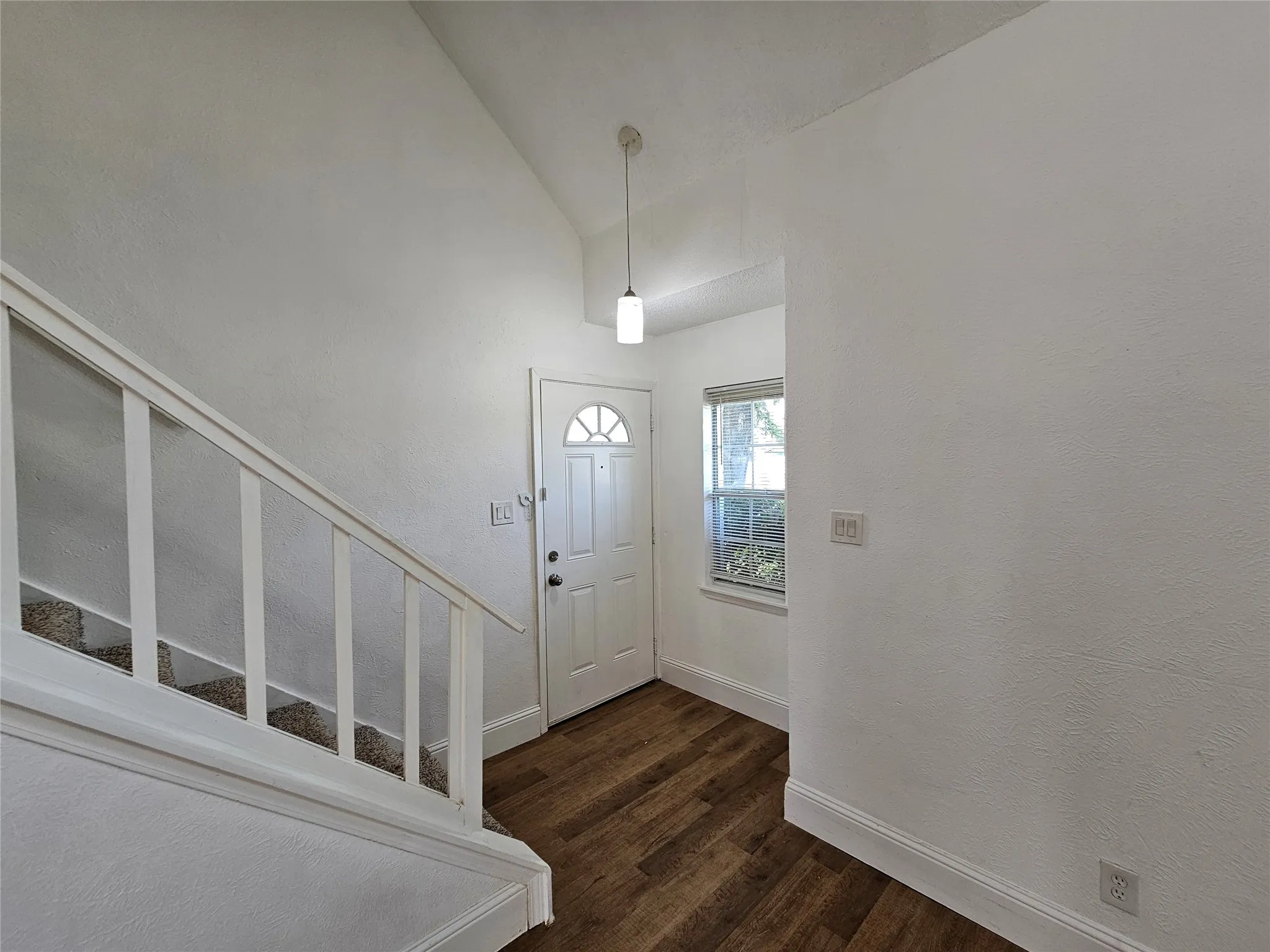 Entryway featuring wood-finish flooring, a white paneled door with a half-moon window, a side window, and a staircase with white railings