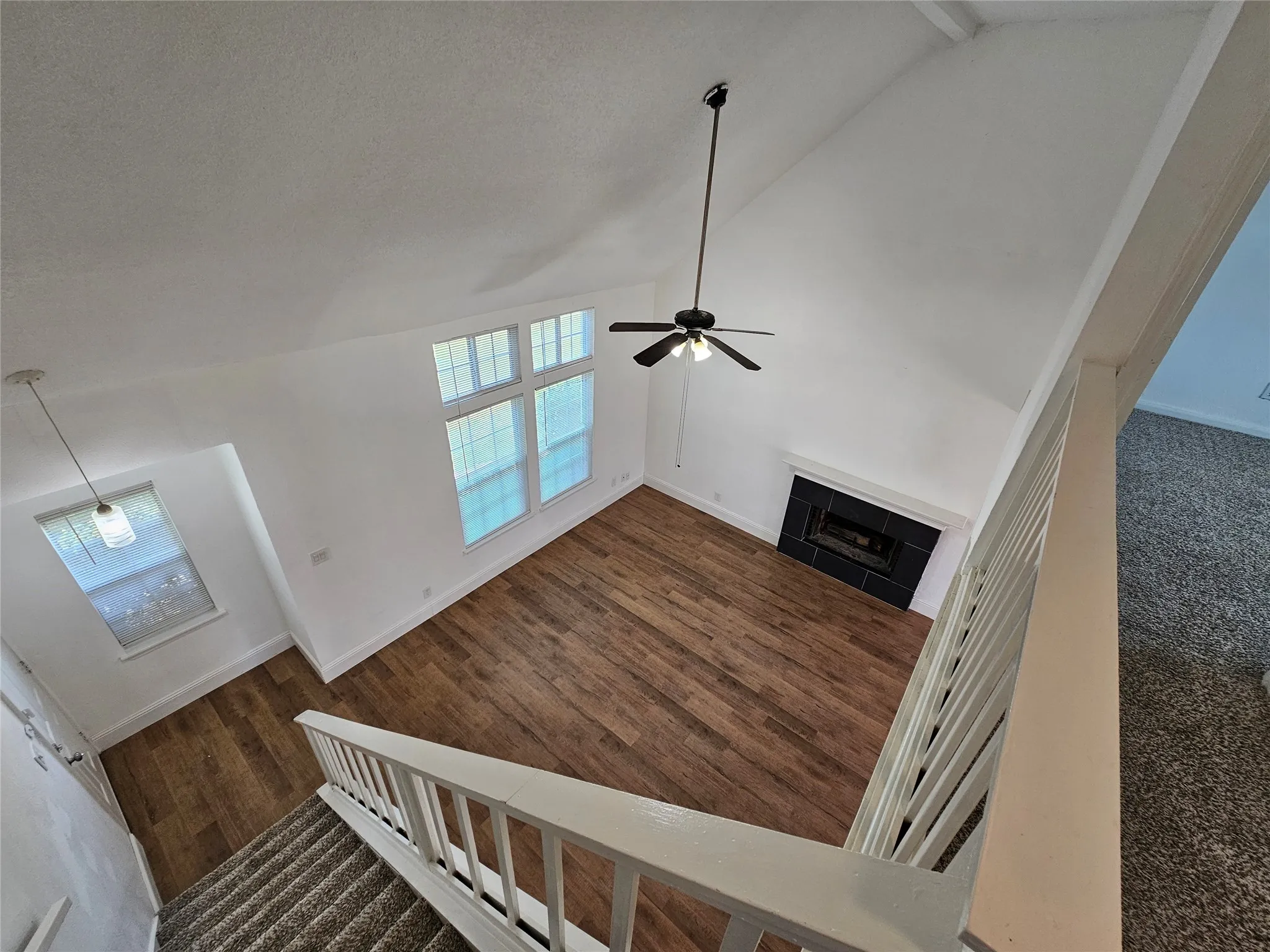 Vaulted ceiling with exposed beams, wood-finish flooring, black tile fireplace, ceiling fan, and multiple windows
