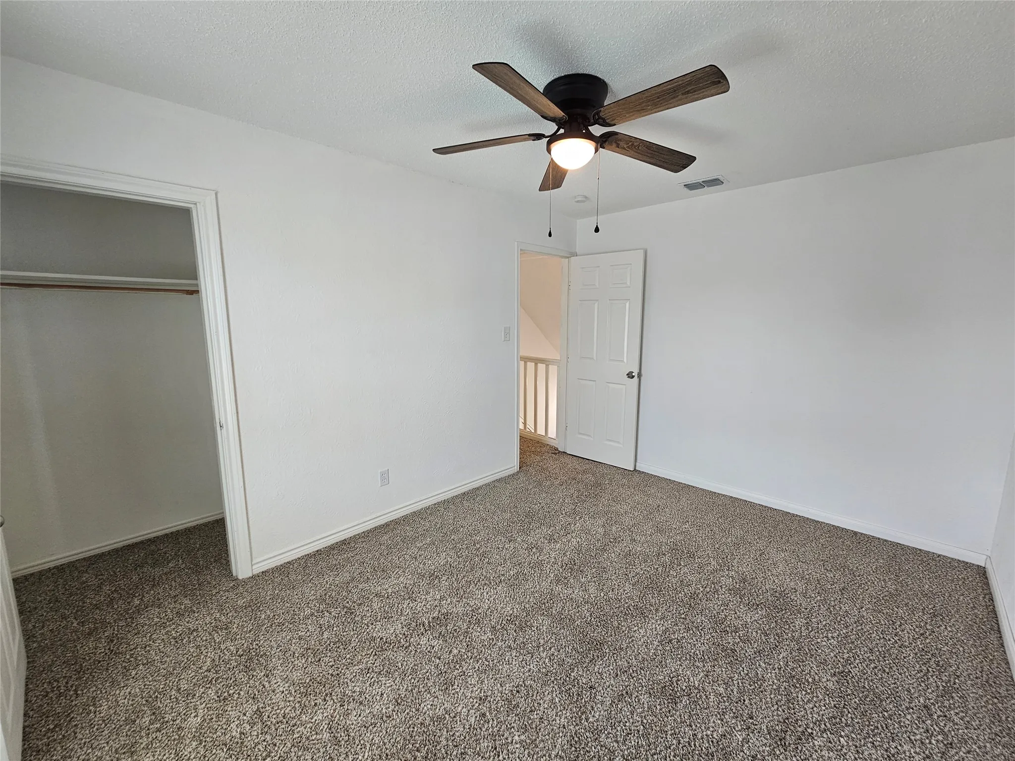Ceiling fan with integrated lighting, neutral-toned carpeting, white painted walls, and an open closet space