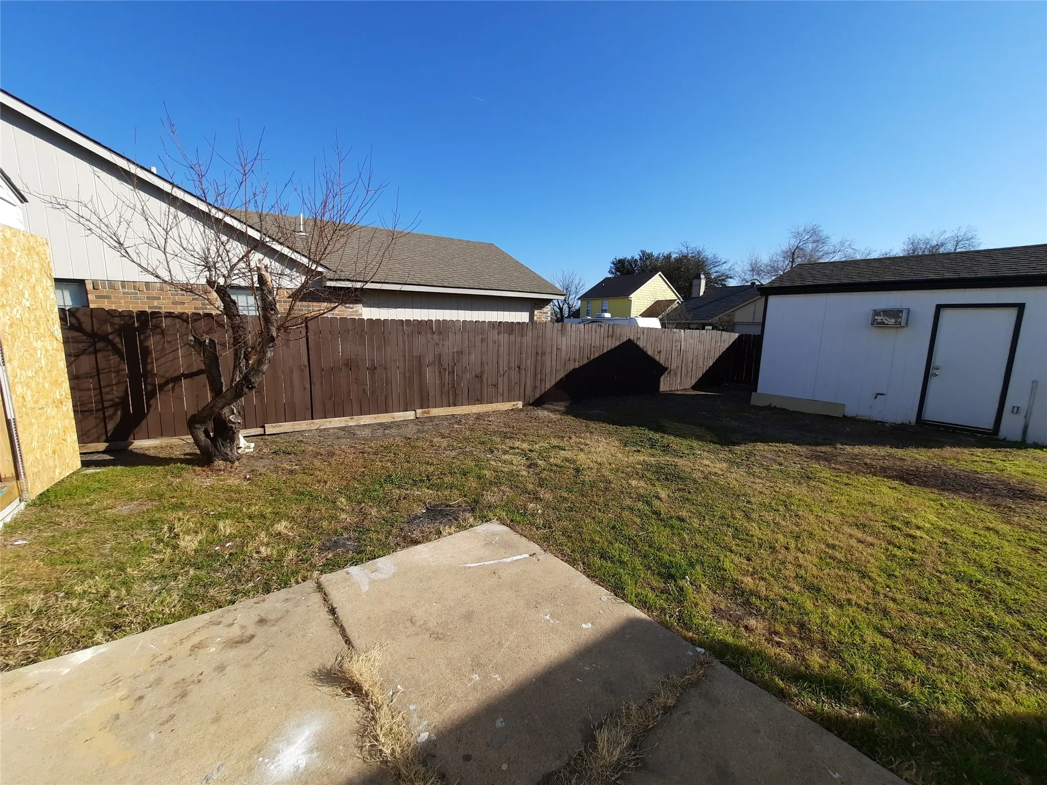Private yard featuring a wood privacy fence, concrete patio, and a storage shed with a white exterior