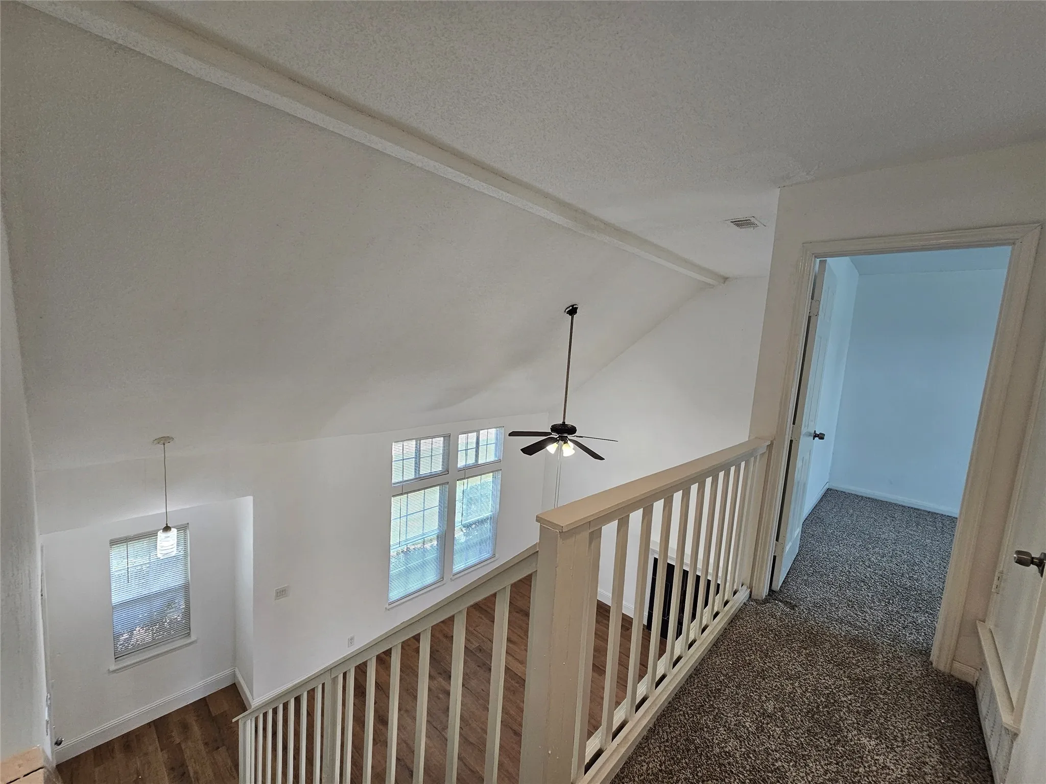 Vaulted ceiling with exposed beam, multiple windows providing natural light, ceiling fan, wood-finish flooring, and carpeted upper level