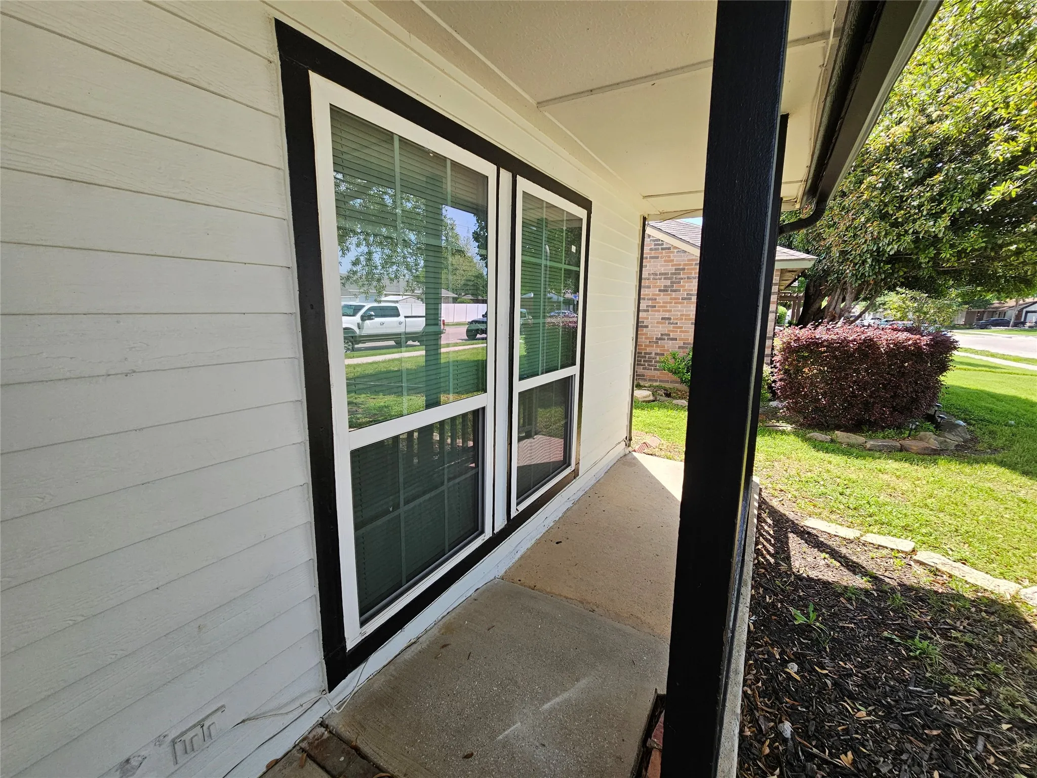 White horizontal siding with black trim, concrete porch, and a landscaped front yard with a mature shrub