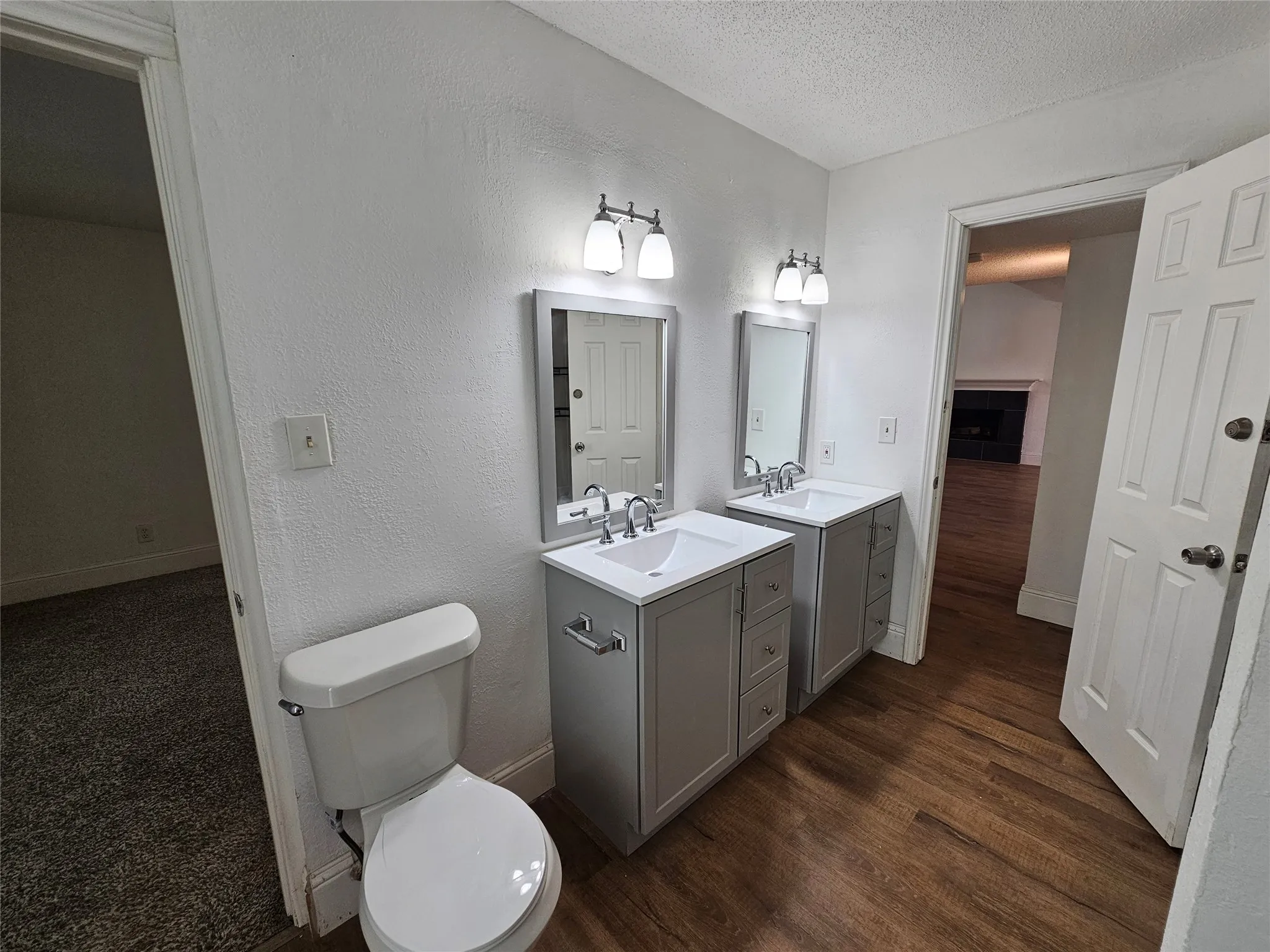 Dual vanity with light gray cabinetry and white countertops, wood-finish flooring, and wall-mounted light fixtures