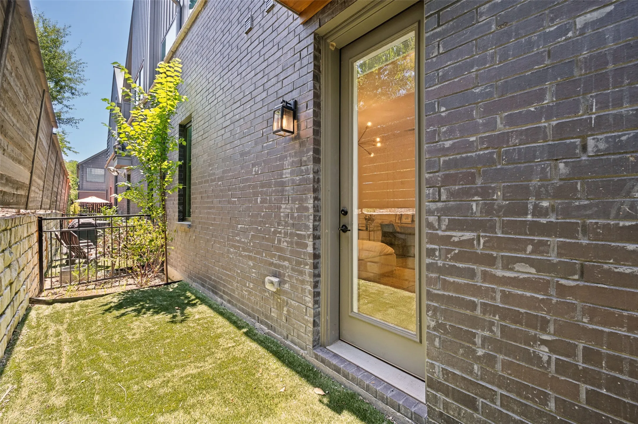 Patio space with artificial turf, bordered by a brick wall and a wood fence